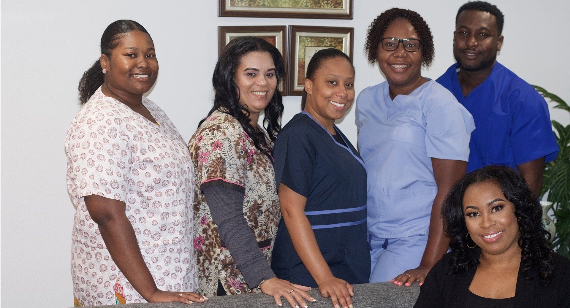 Group of six people posing; some in scrubs, others in casual wear; in a medical office setting. Group of six people posing; some in scrubs, others in casual wear; in a medical office setting.