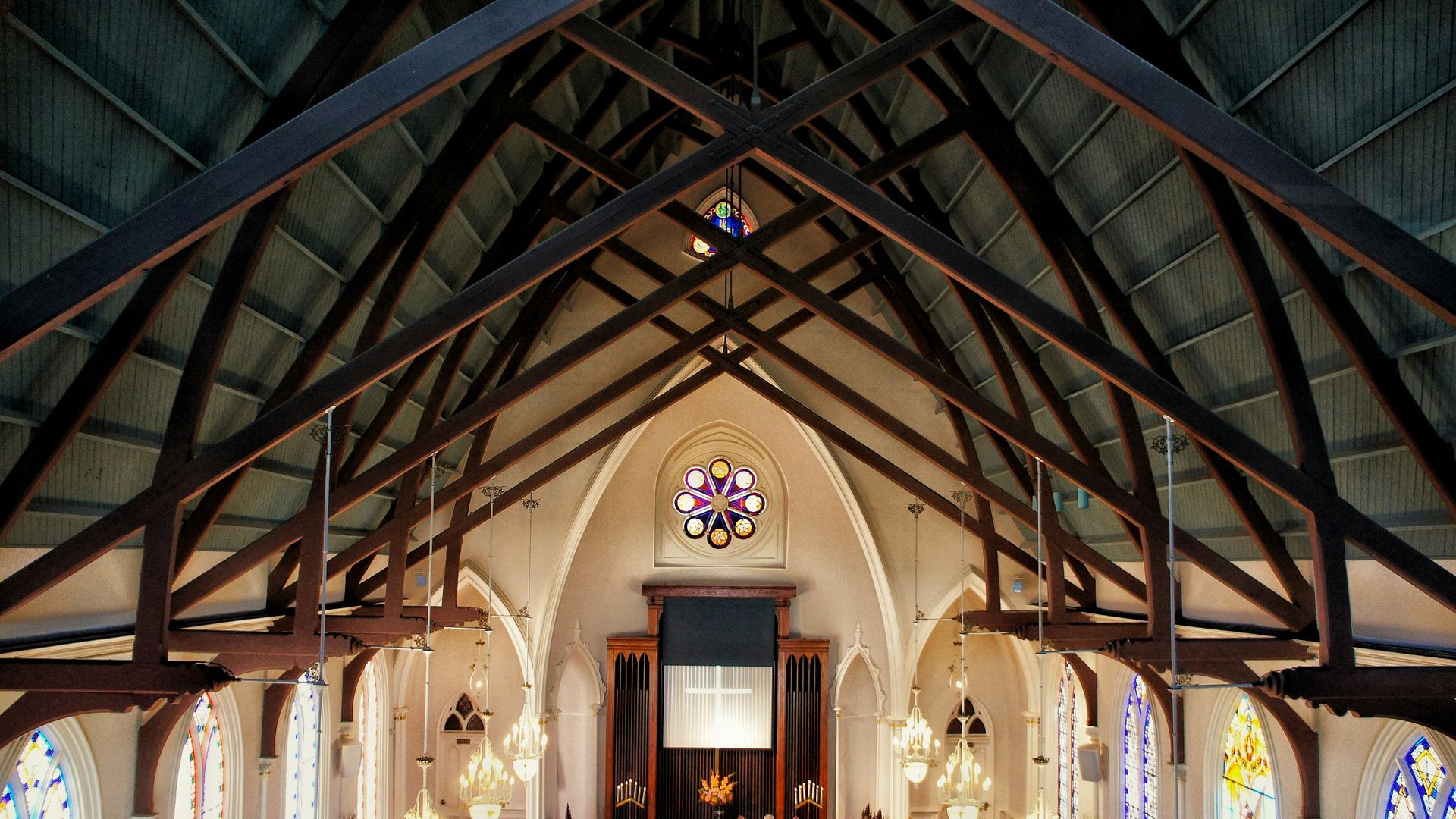 Interior of a church with wooden beams, arched ceilings, stained glass, and an ornate altar.