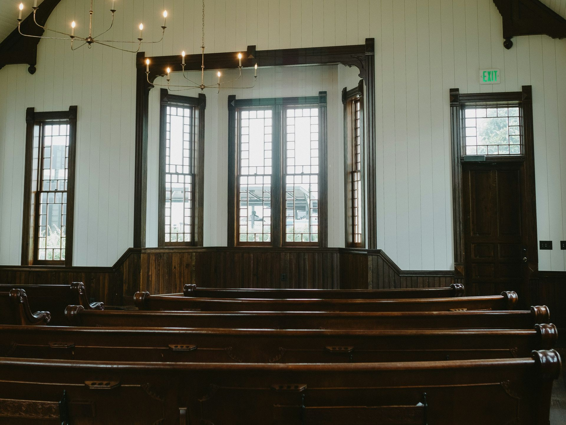 Wooden interior with pews facing large windows. Brown trim, white walls.