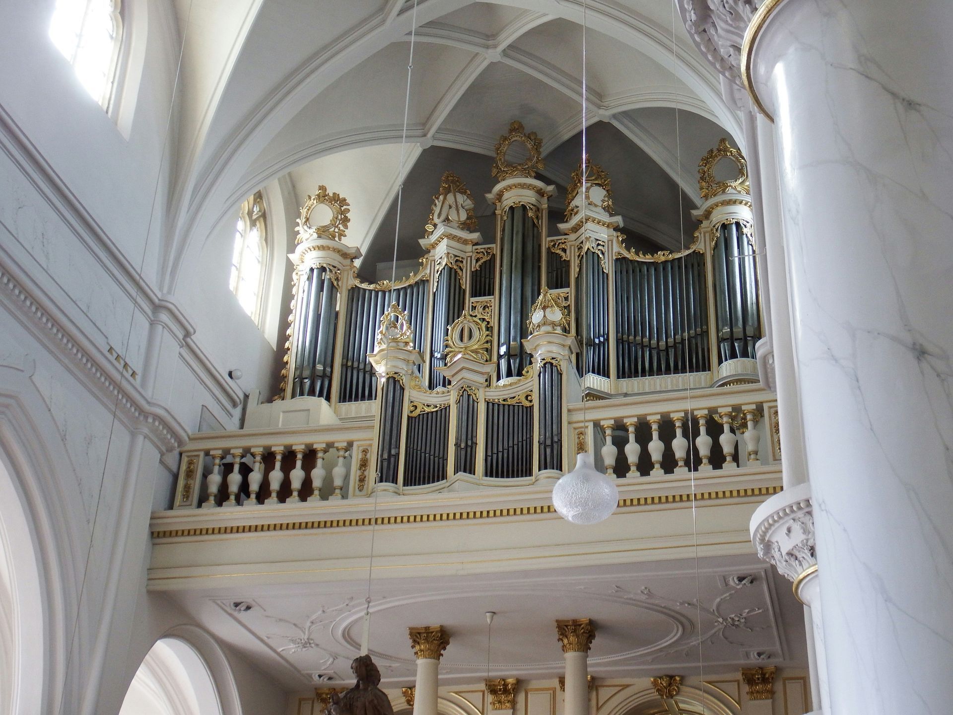 Interior of a church with rows of wooden pews facing an open doorway to a grassy area. Bright natural light.
