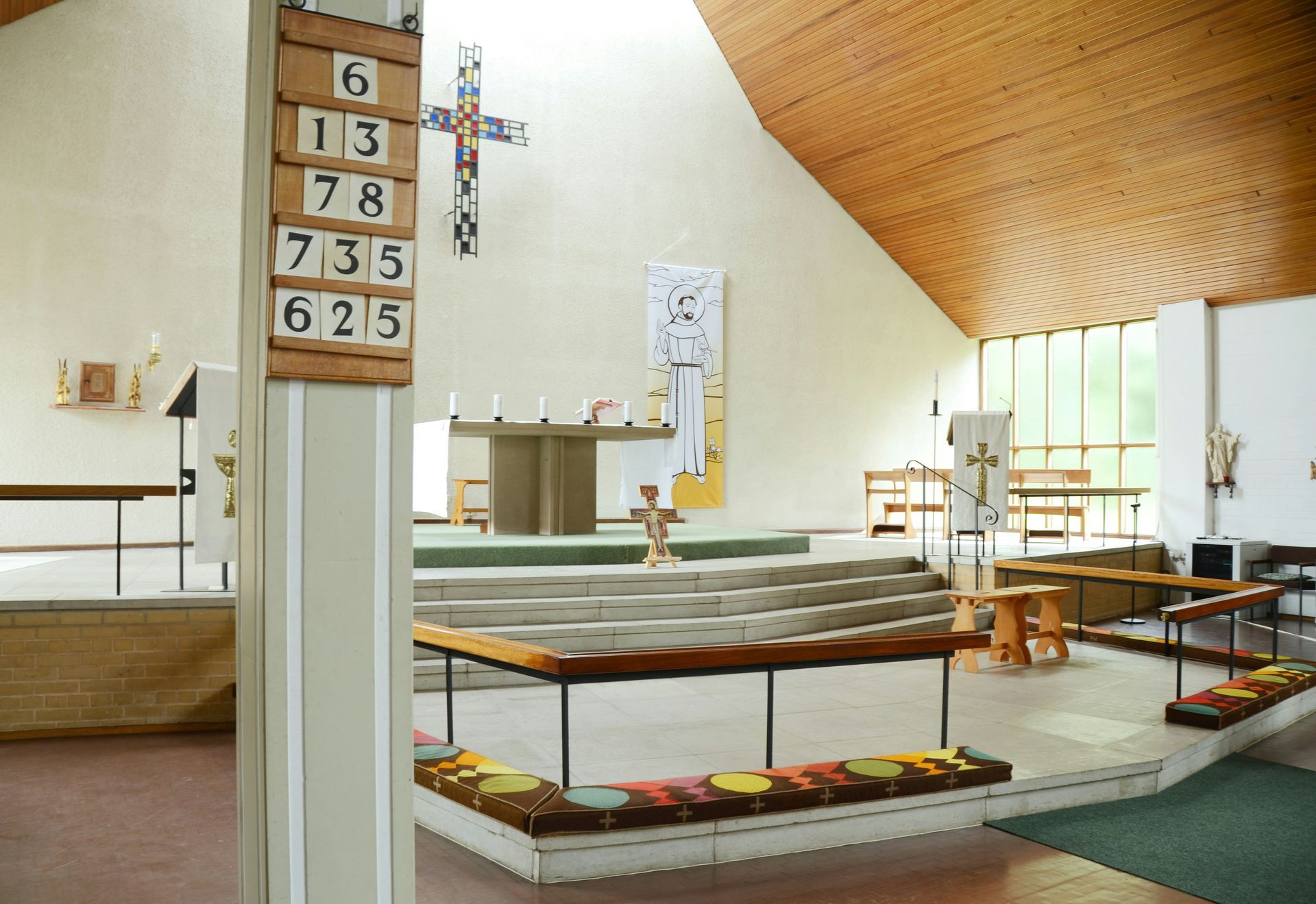 Interior of a church with a wooden ceiling, altar, and pews. A cross hangs above the altar.