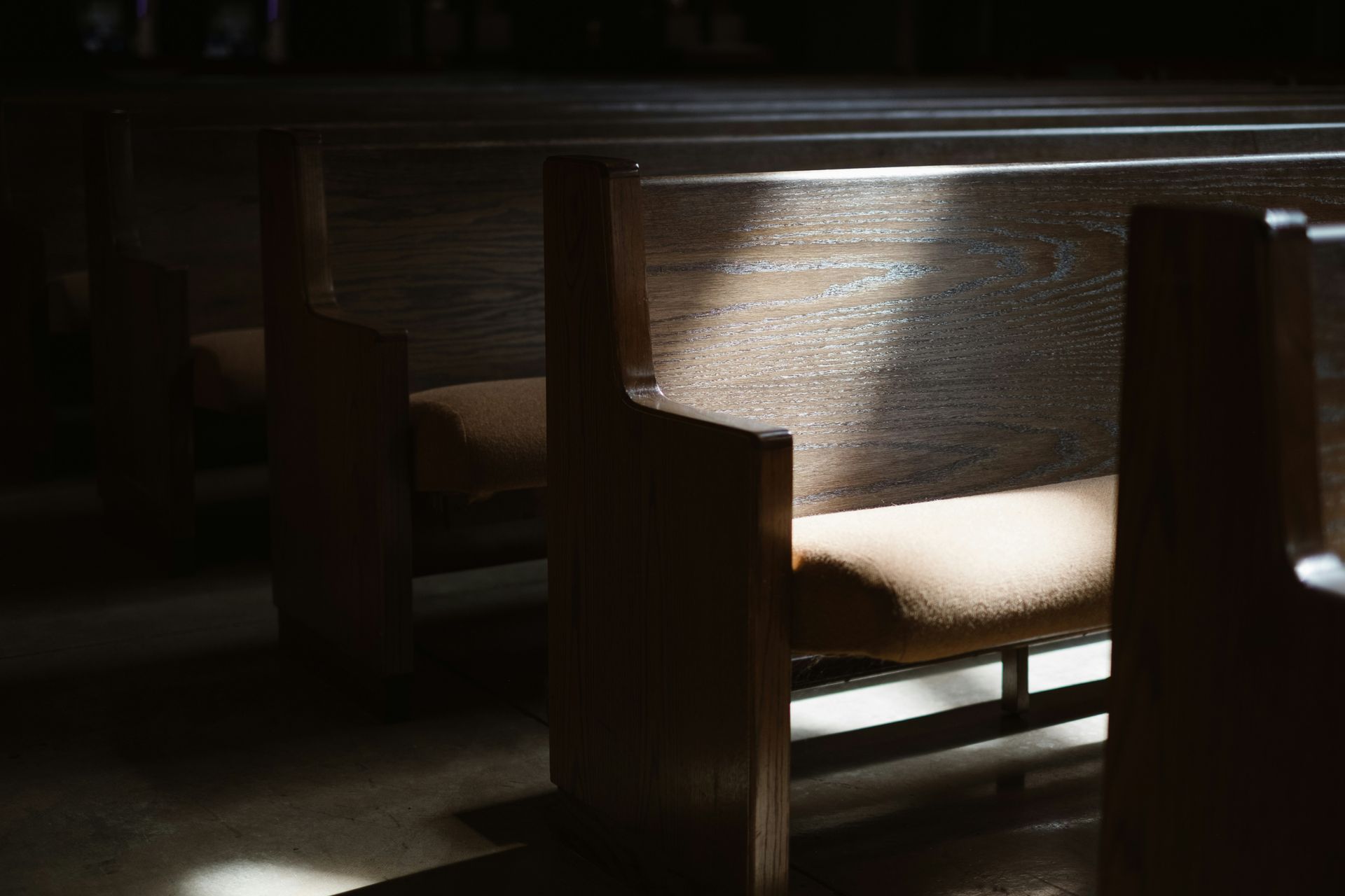 Wooden church pews in a dimly lit room, with a beam of light shining across them.