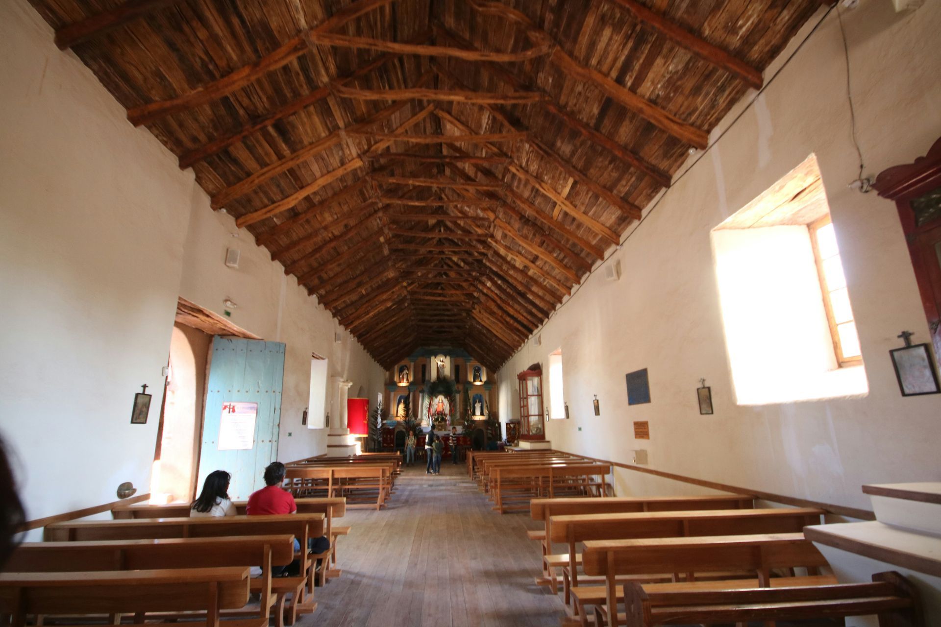 Interior of a historic church in Boise with wooden benches, white walls, and a thatched roof. People are present.