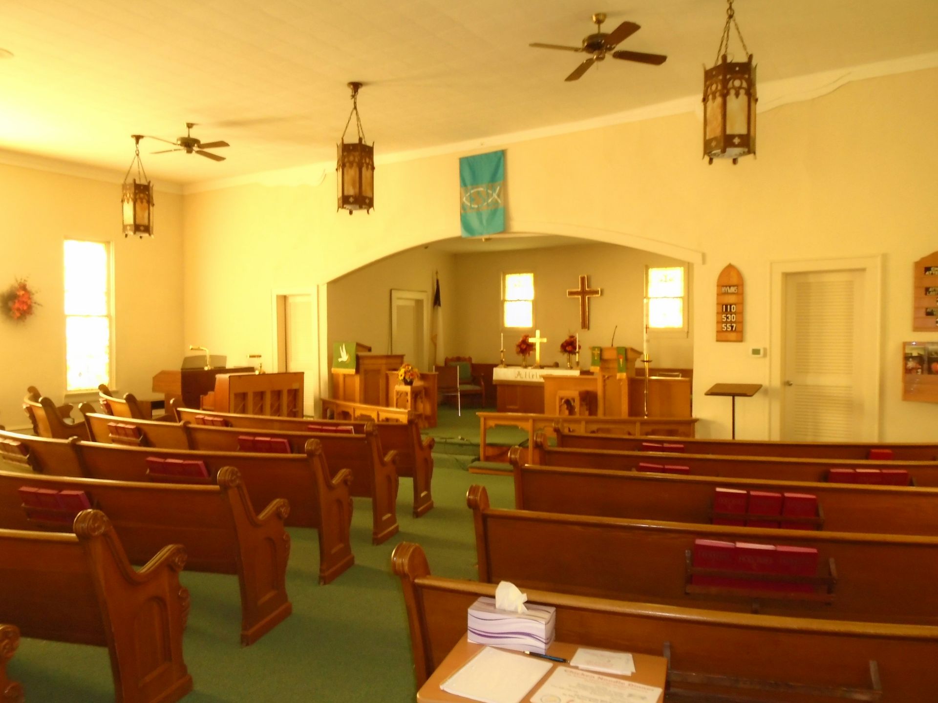 Interior of a church sanctuary with wooden pews, altar, and hanging lamps.