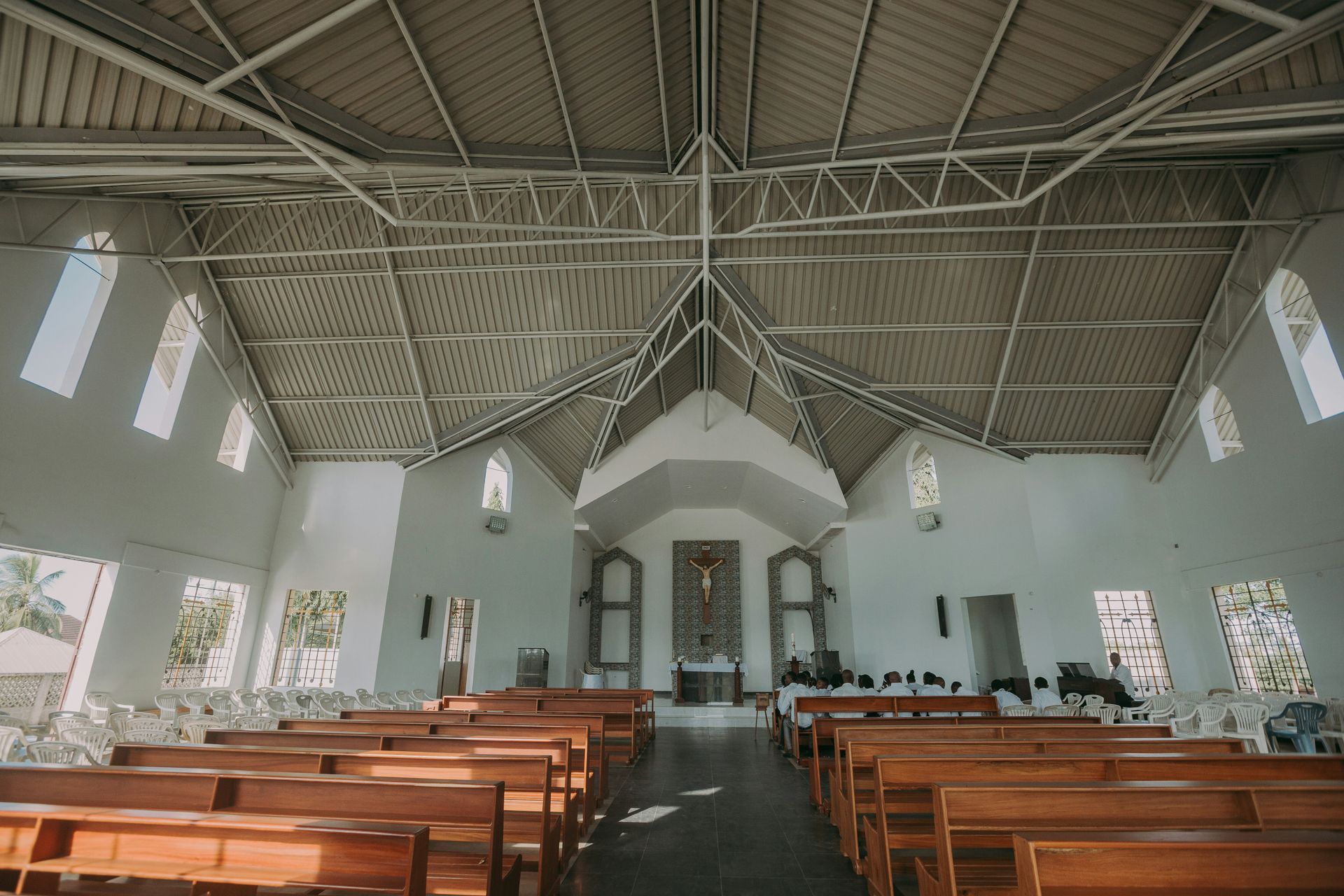 Inside a church with rows of wooden pews, white walls, and a high, angled metal ceiling.
