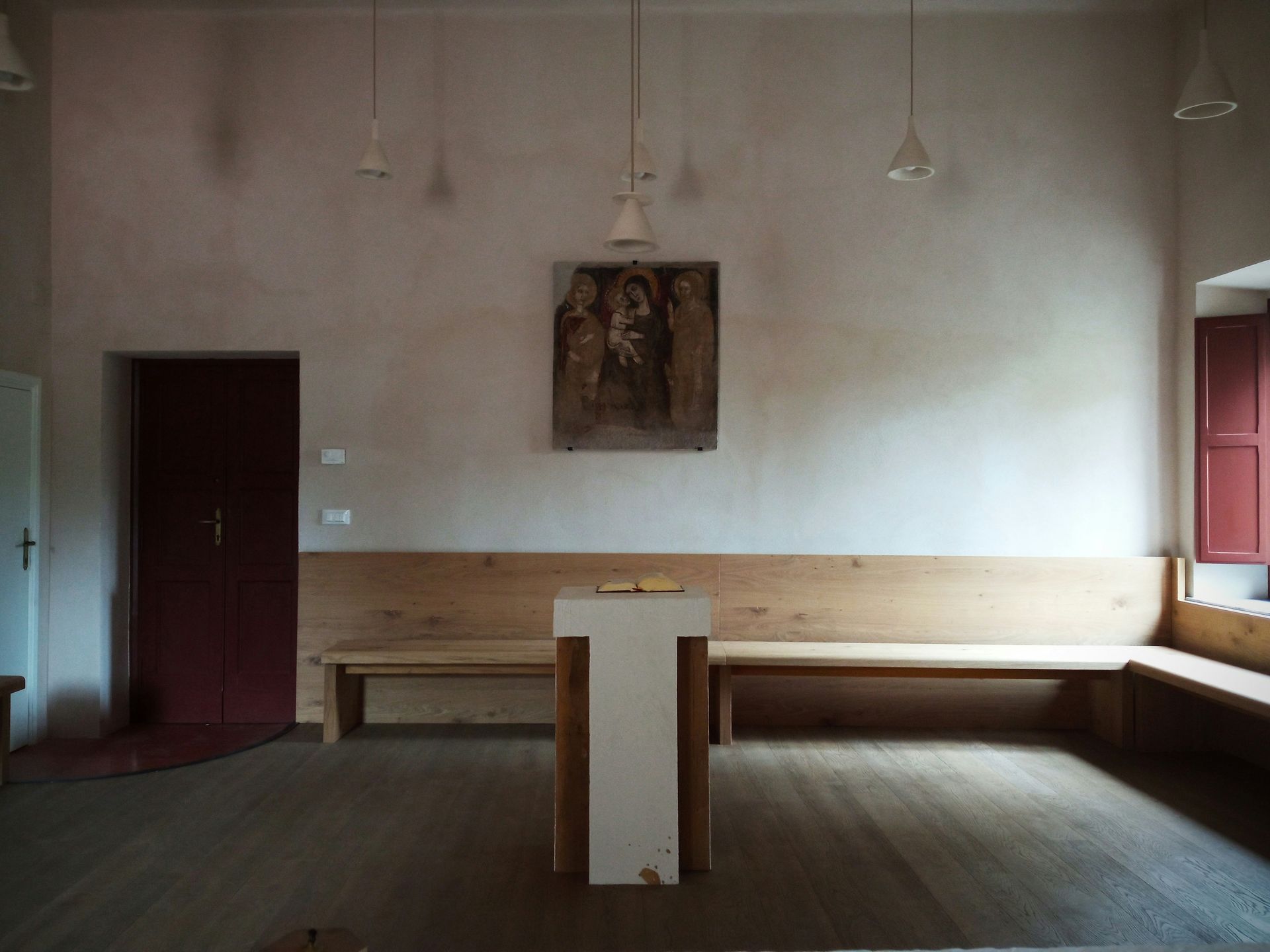 Interior of a church with rows of wooden pews facing an open doorway to a grassy area. Bright natural light.