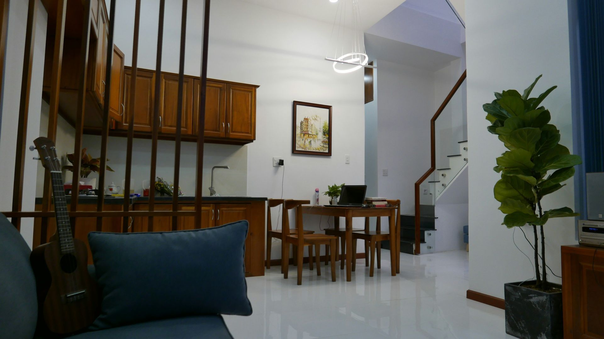 Living room with wooden kitchen, dining set, stairs, and potted plant.