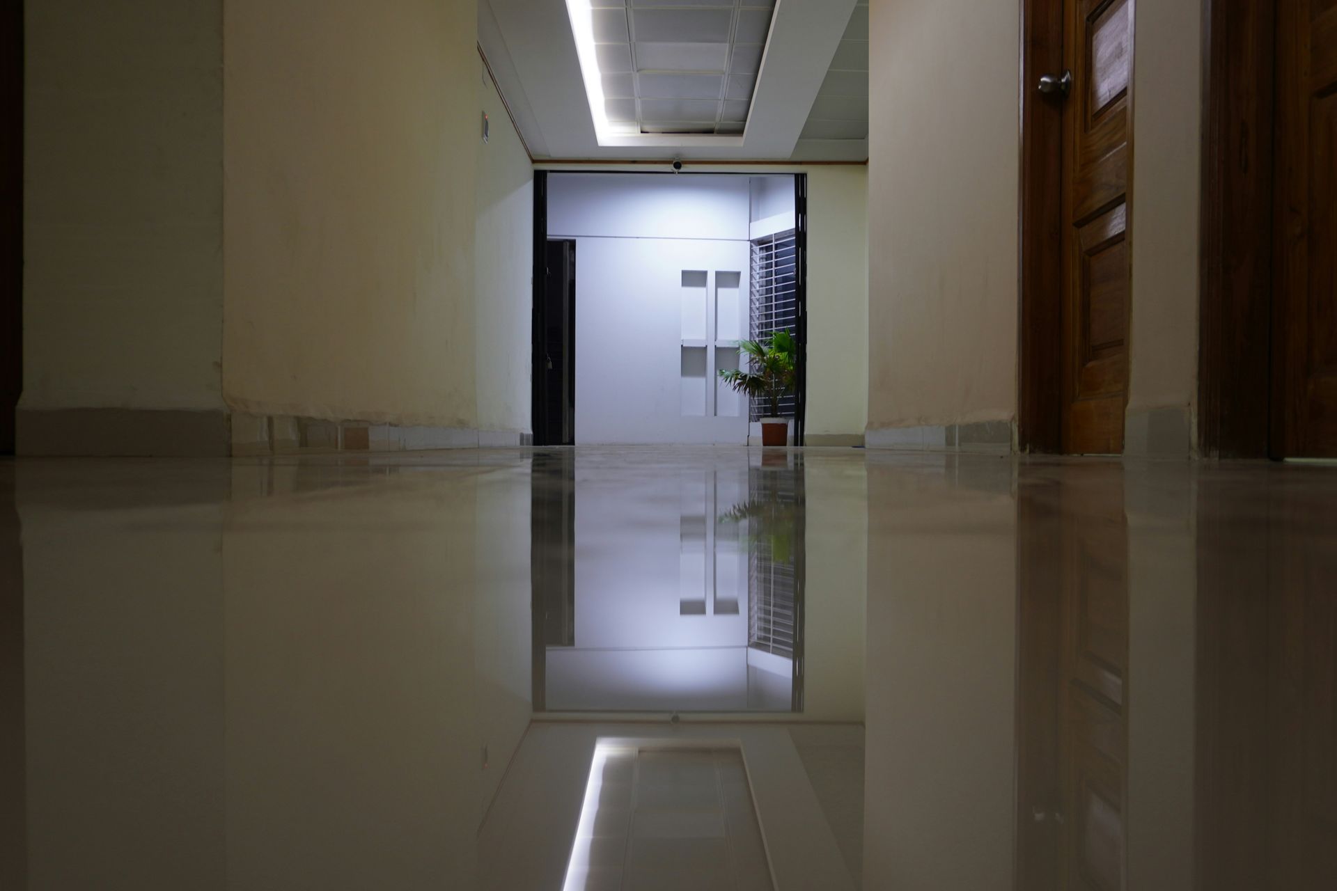 Hallway with polished floors, walls, doors, and a bright light at the end.