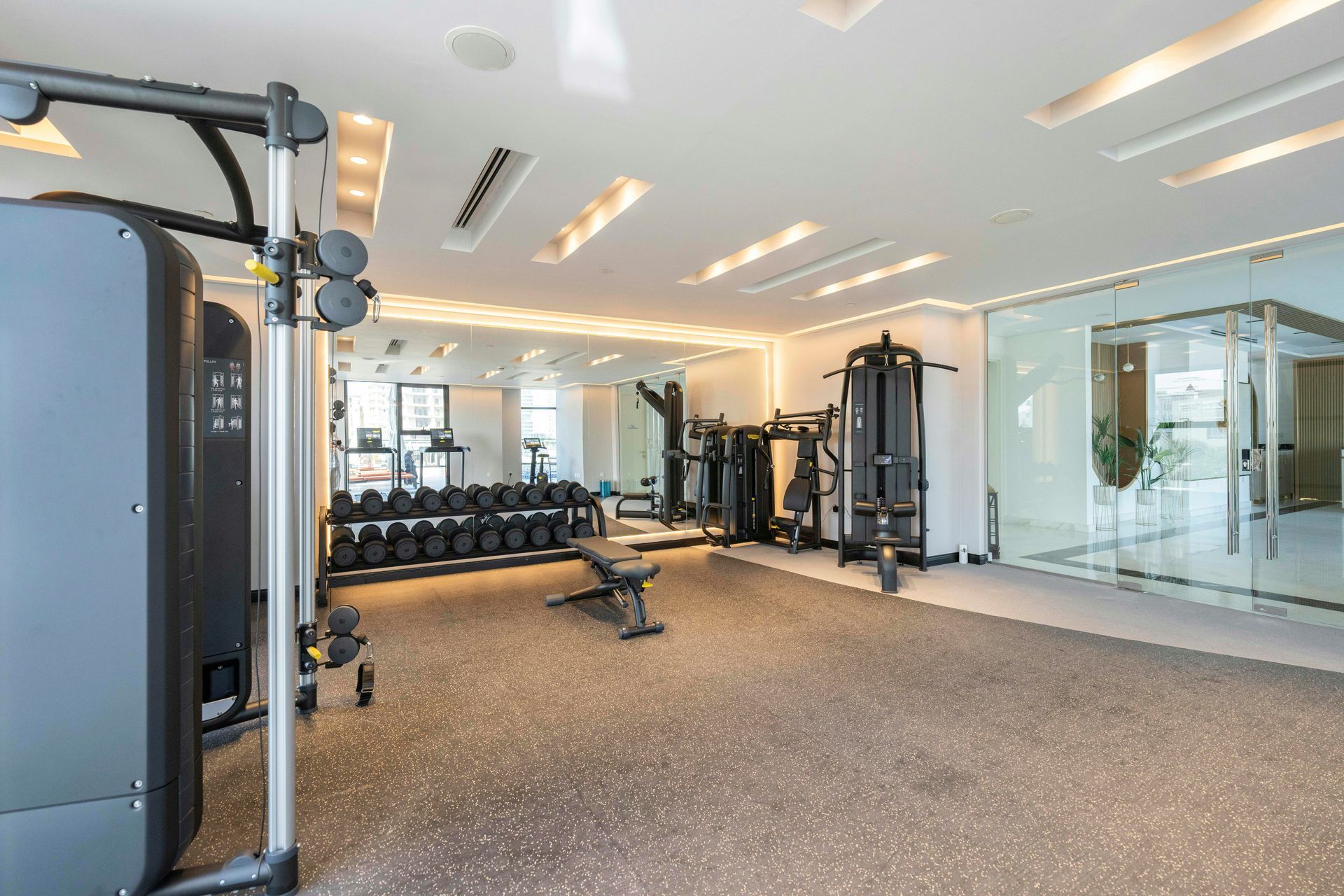 Gym with weight machines, dumbbells, bench, mirror, and rubber flooring.