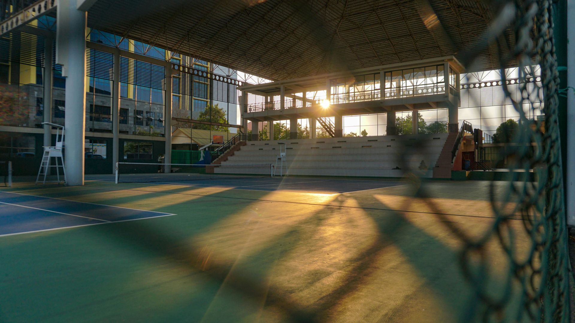 Outdoor sports court with sunlight filtering through a structure; a person walks in the distance.