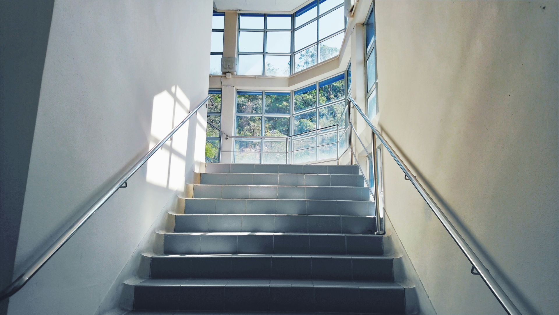 Staircase leading up to a glass-walled area, bright sunlight illuminating the steps and walls.