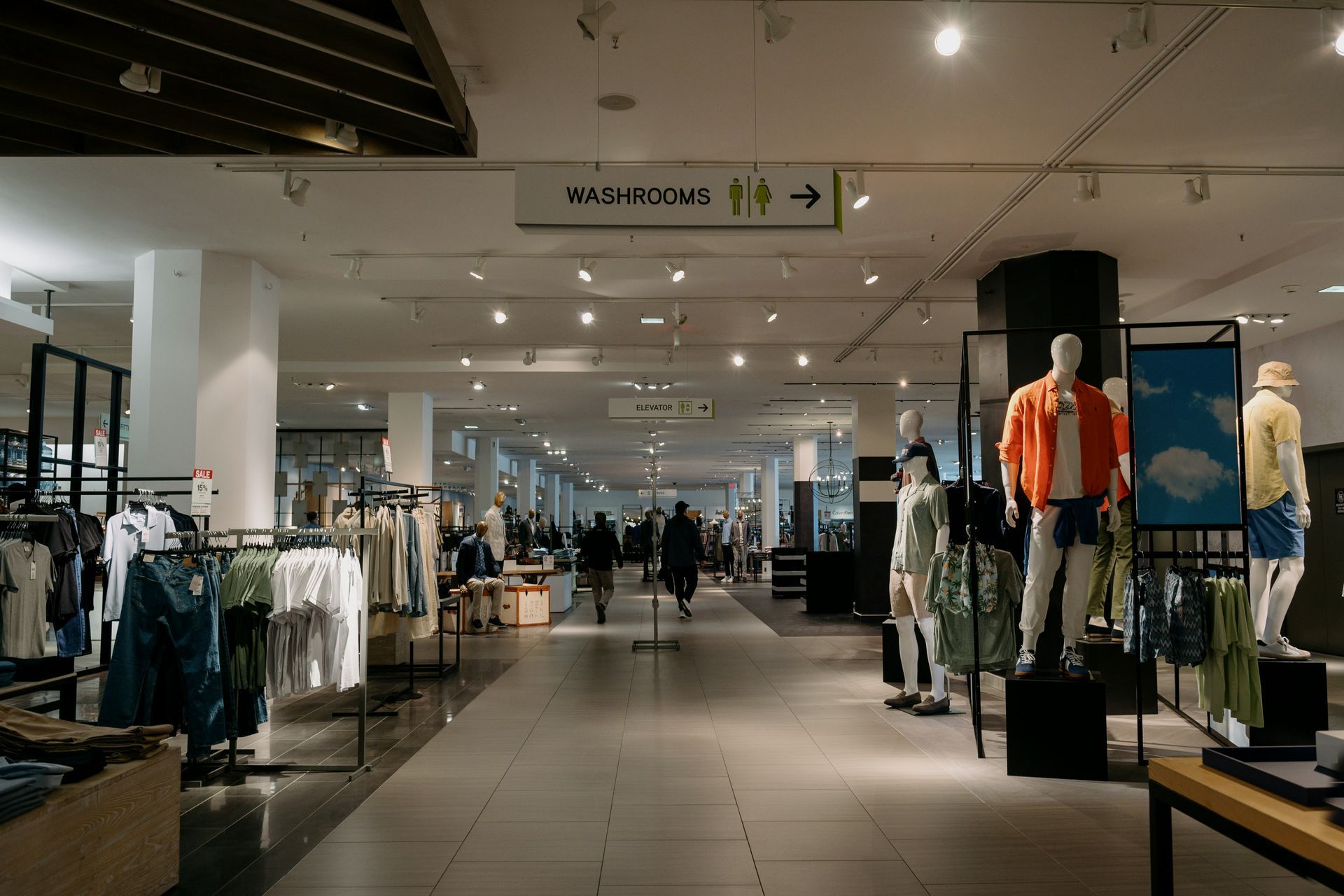 Inside a department store, clothing racks and mannequins. People walking in the aisles.