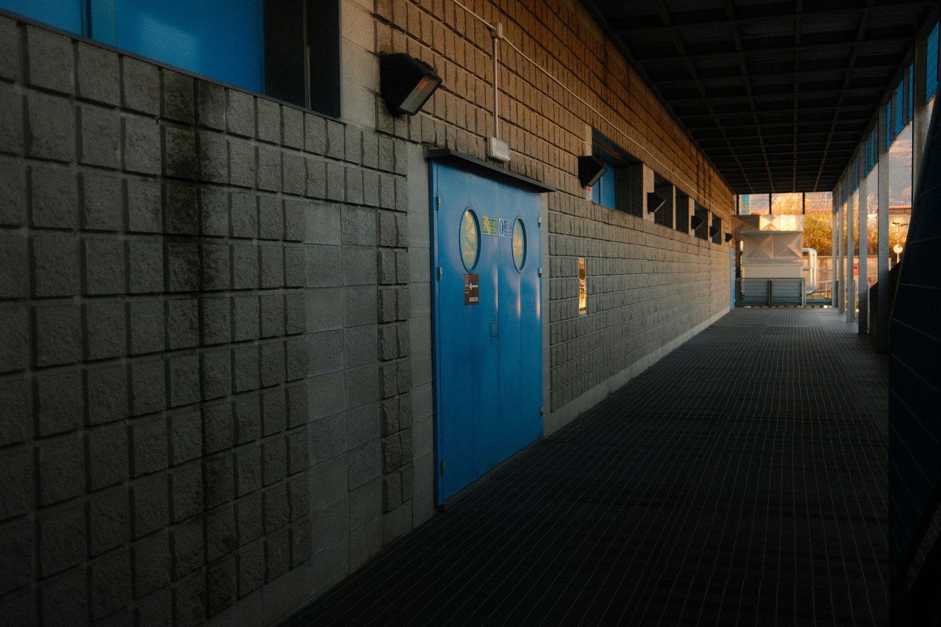 Blue door in a concrete block hallway, lit by sunlight.