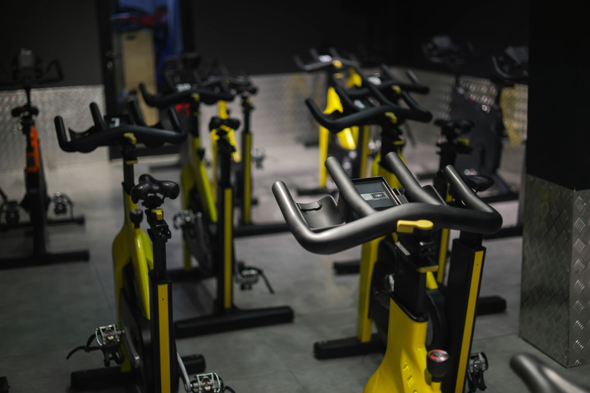 Indoor cycling bikes in a gym, with yellow frames, black handlebars, and digital displays.
