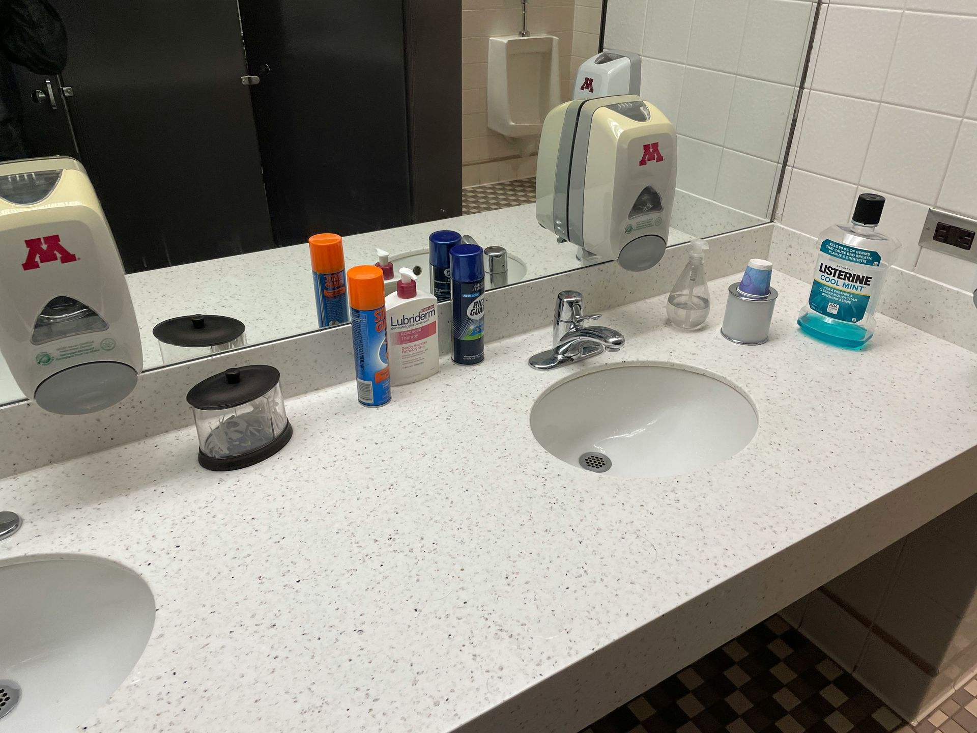 Public restroom with sinks, mirrors, soap dispensers, and various toiletries.