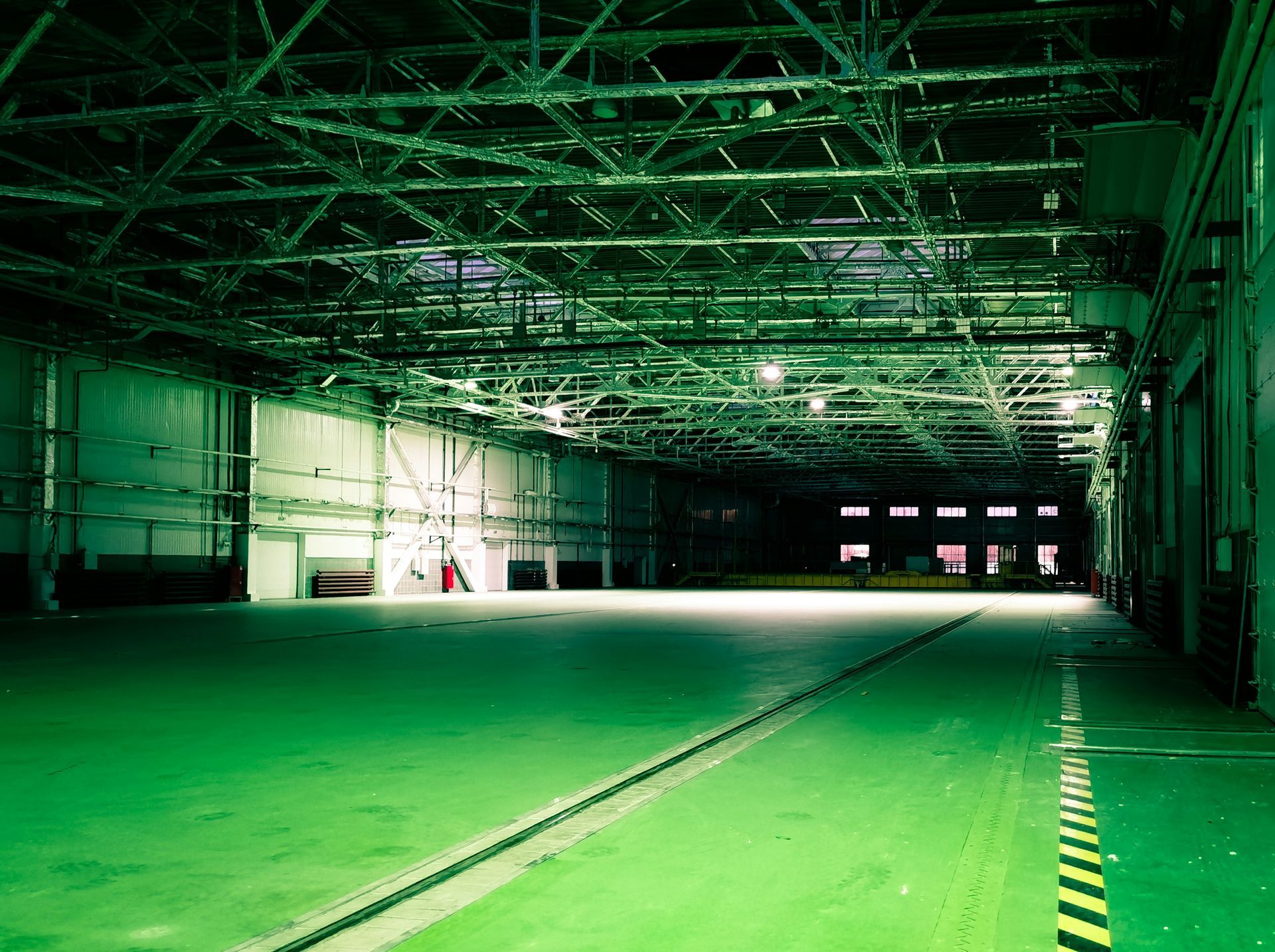 Empty warehouse with green lighting; vast, open space; industrial setting.