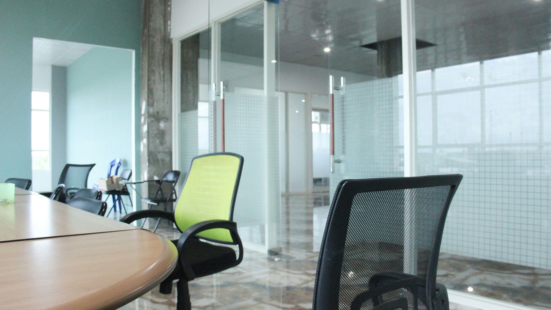 Office interior with round table, office chairs, and glass-walled rooms; light green and black chairs.