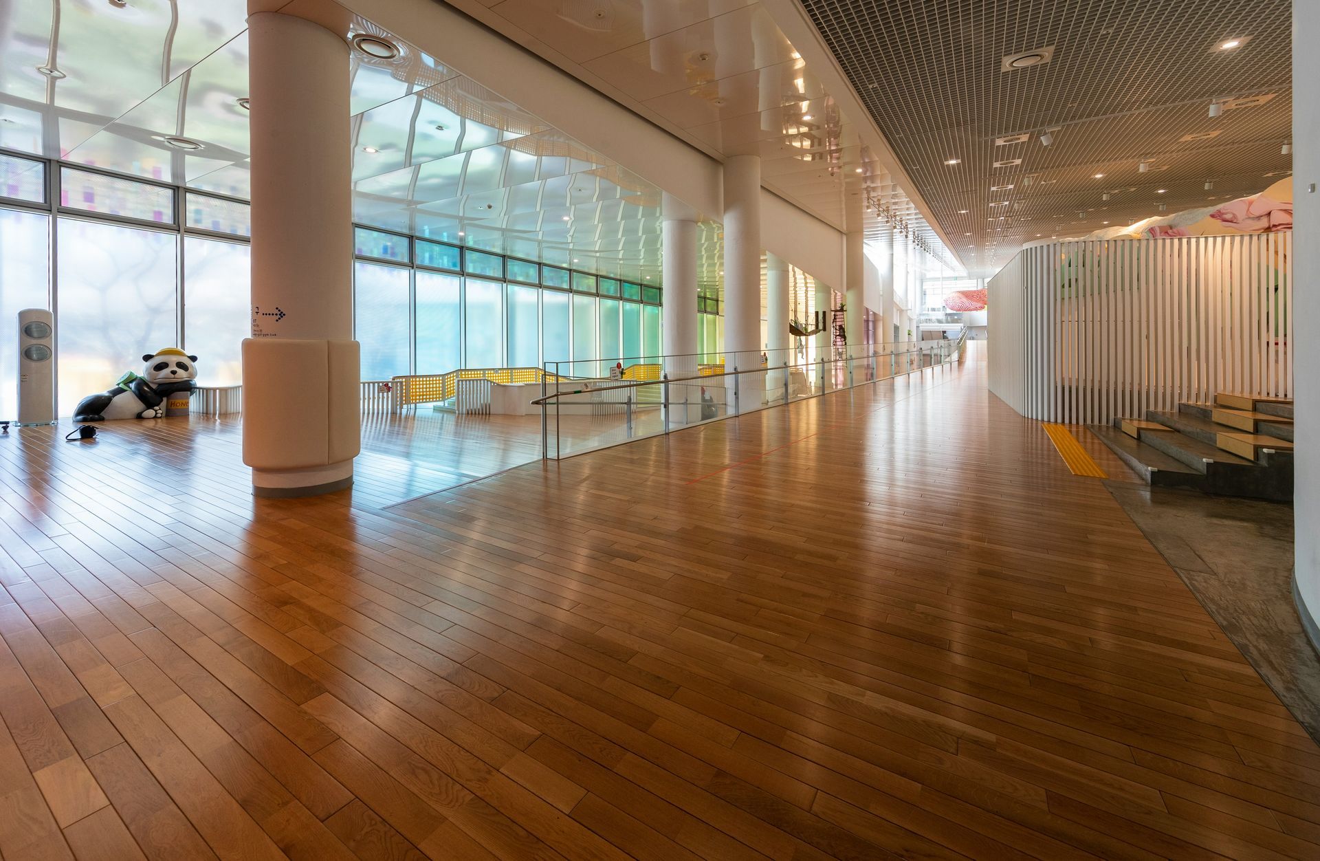 Interior of a library with tables, chairs, computers, and bookshelves. Sunlight streams through windows.