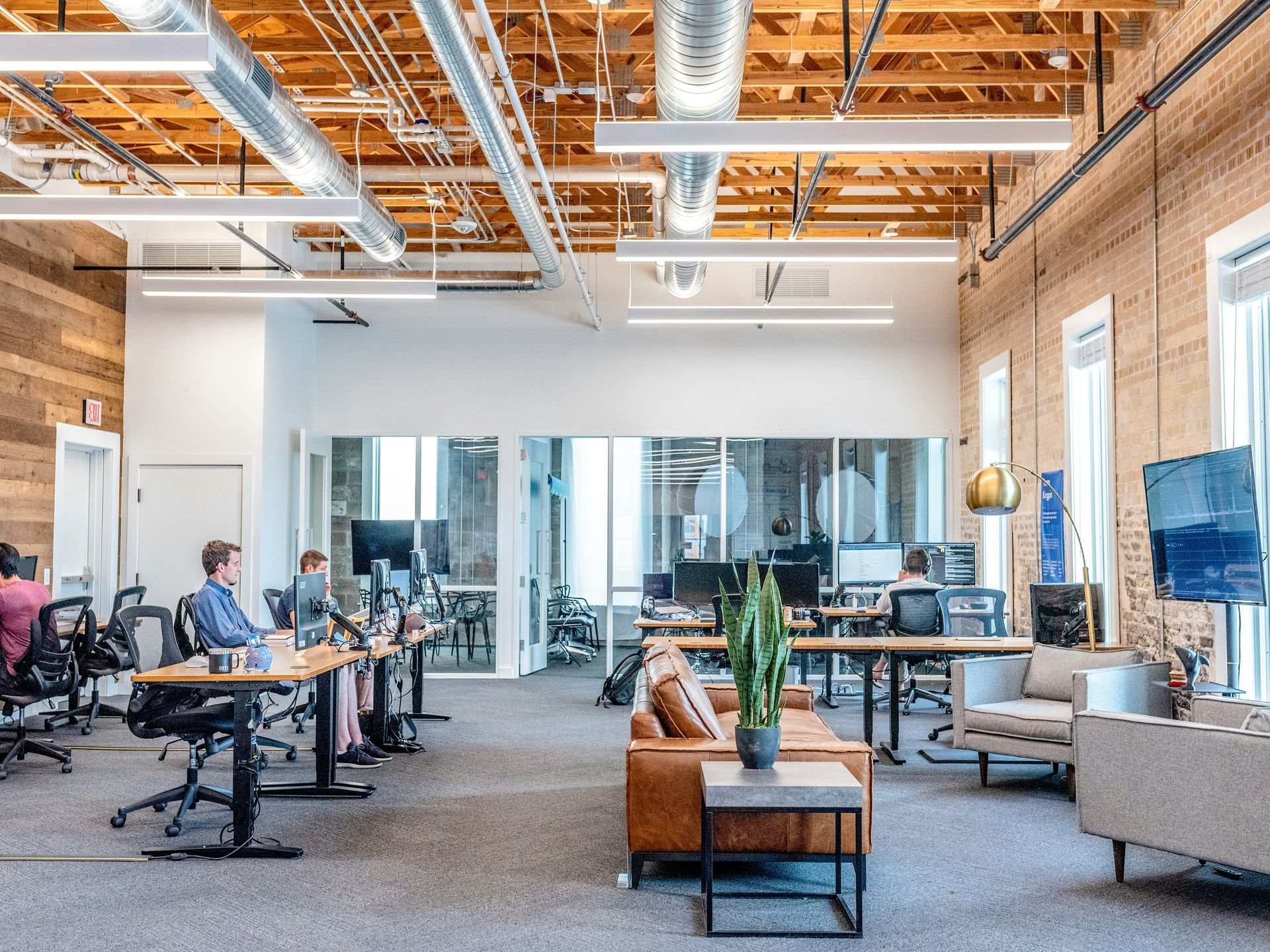 Open-plan office space with desks, exposed beams, and employees working on computers.