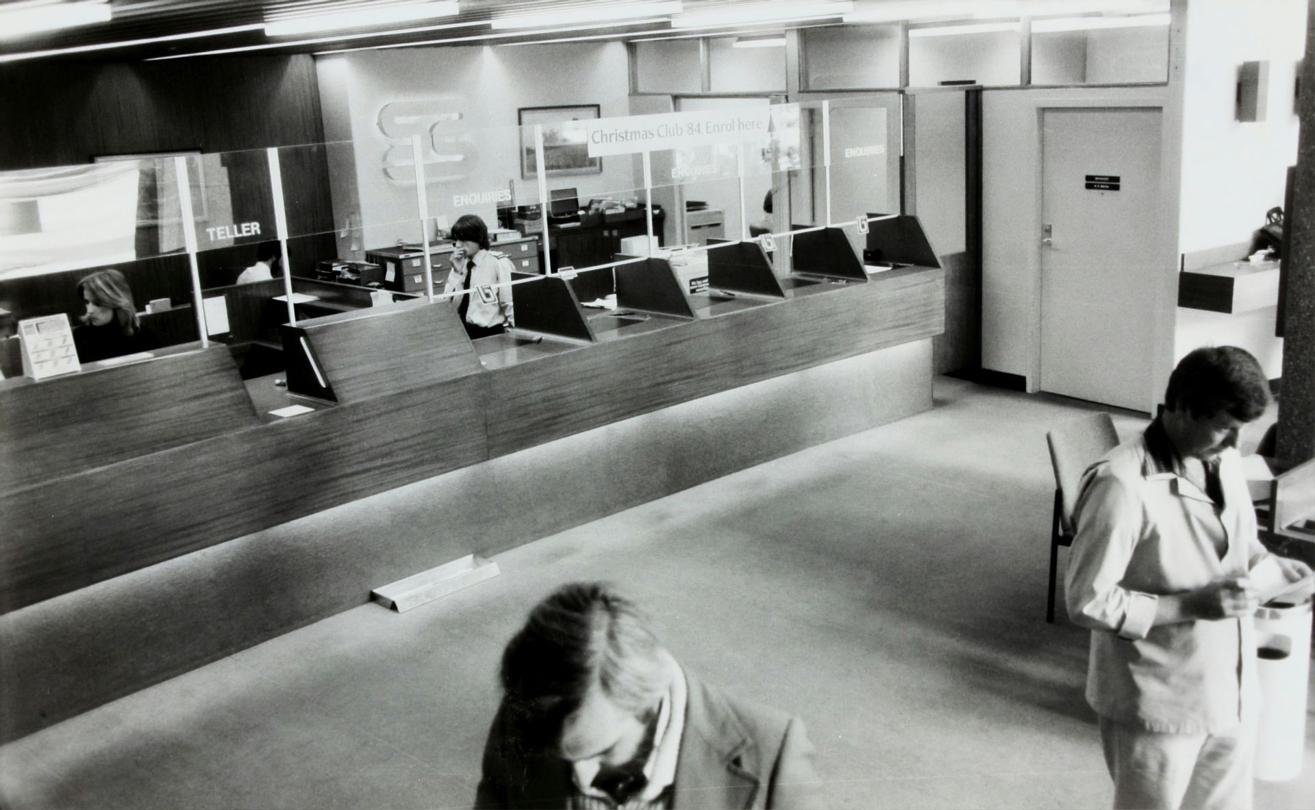 Bank teller booths with brass rails and globe lamps, interior shot.