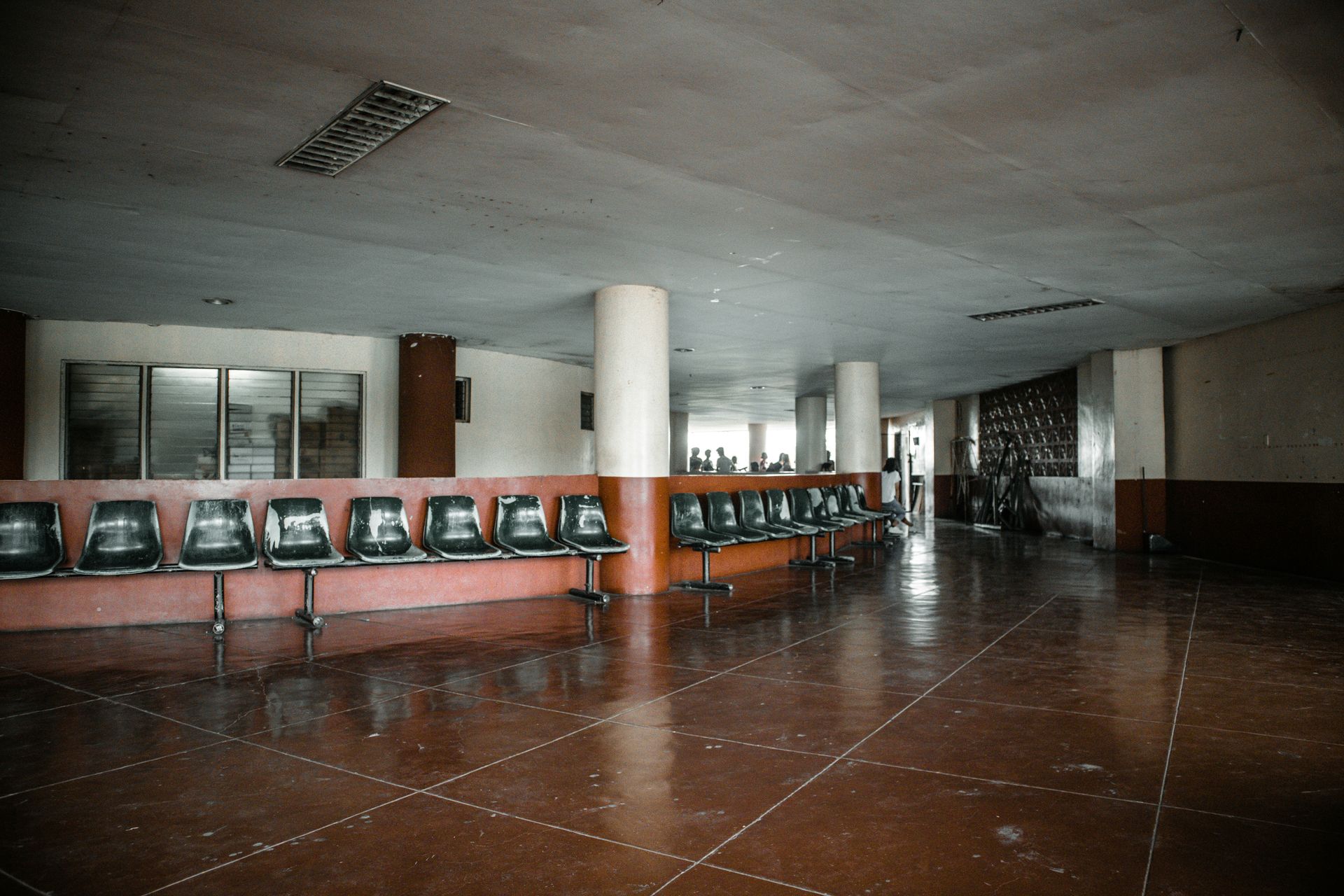 Awaiting area with rows of chairs, red flooring, white columns, and a muted color scheme.