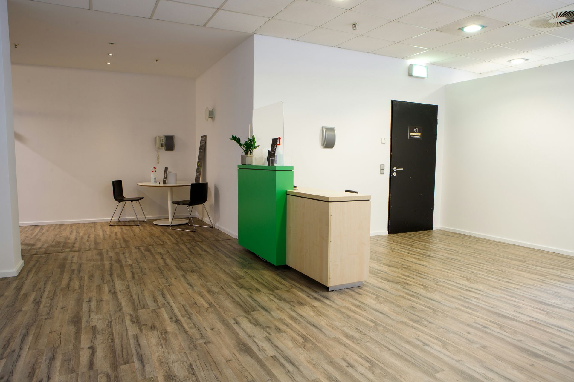 Empty office reception area with a green and beige desk, wooden floors, and white walls.