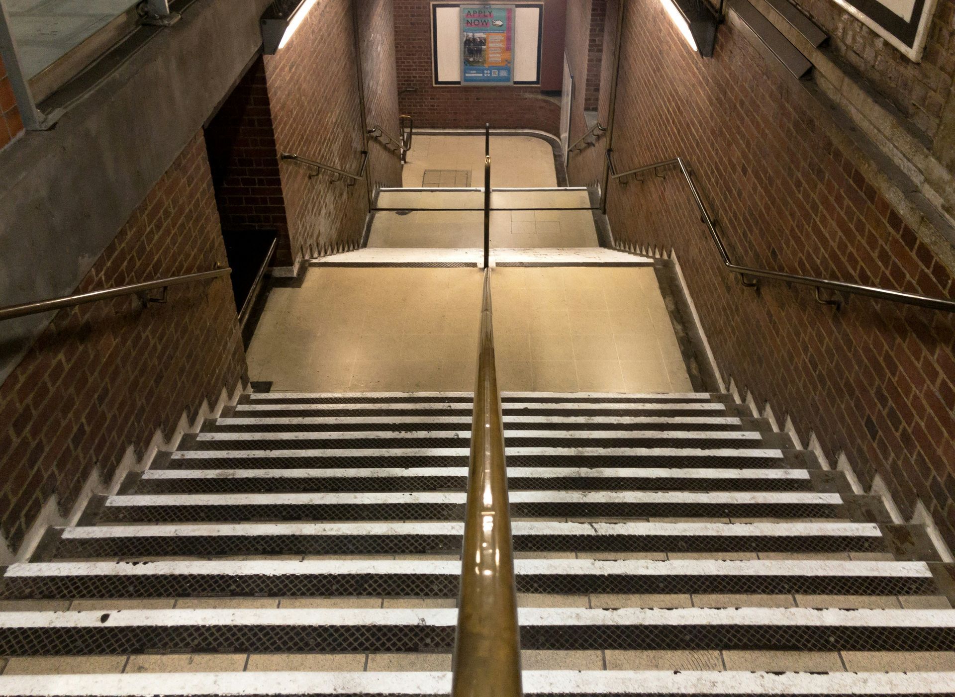 Staircase descending into a subway station. Brown brick walls with metal handrails.