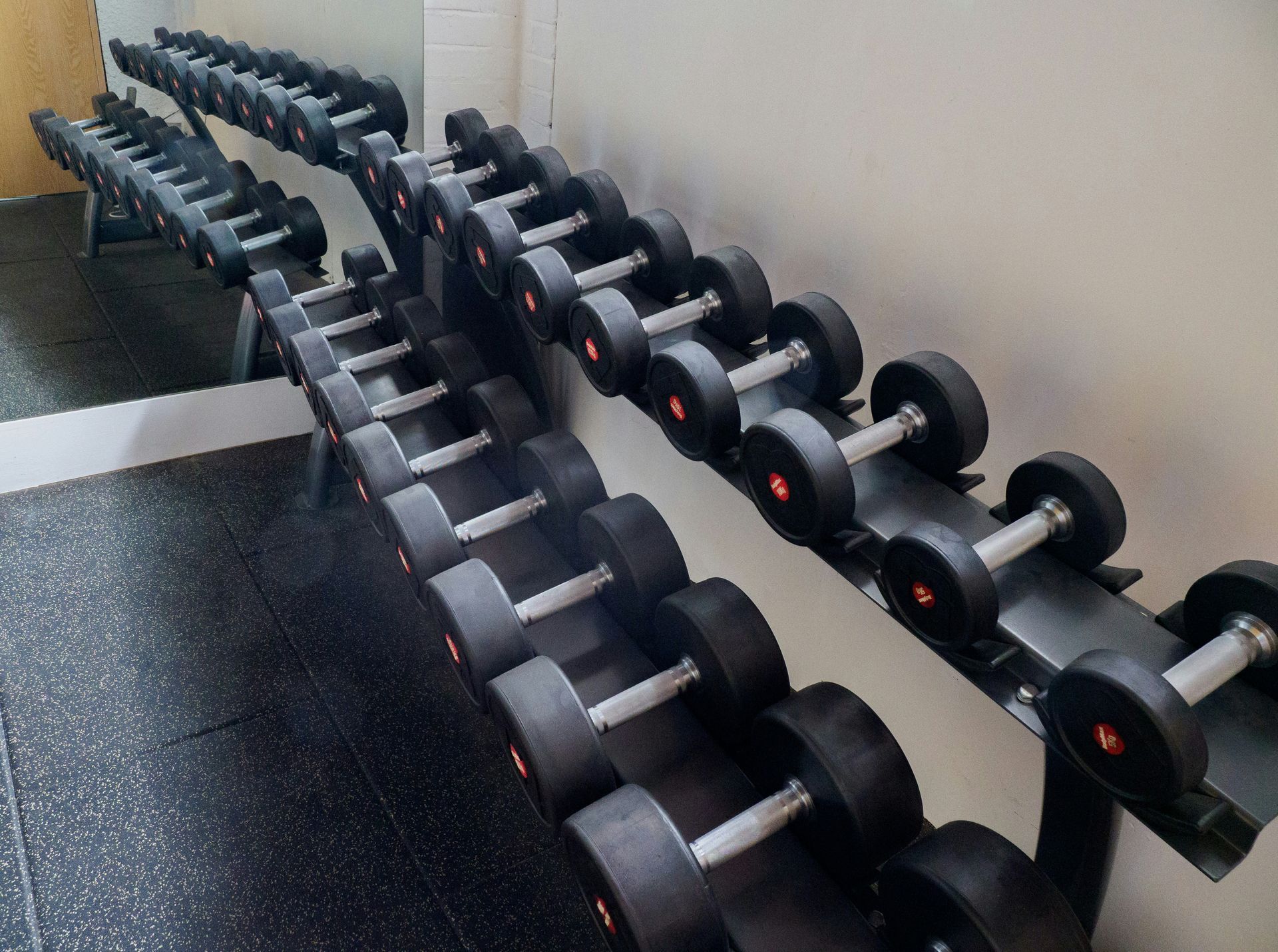 Dumbbells on a rack in a gym. Black rubber weights and black metal rack.