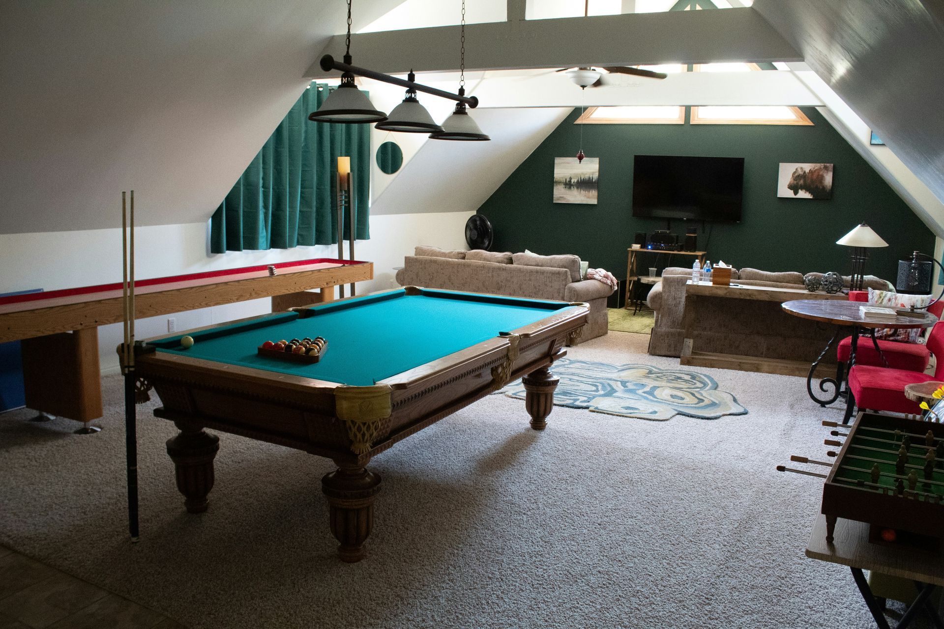 Pool table in a recreation room with a second pool table, sofas, TV, and foosball table.