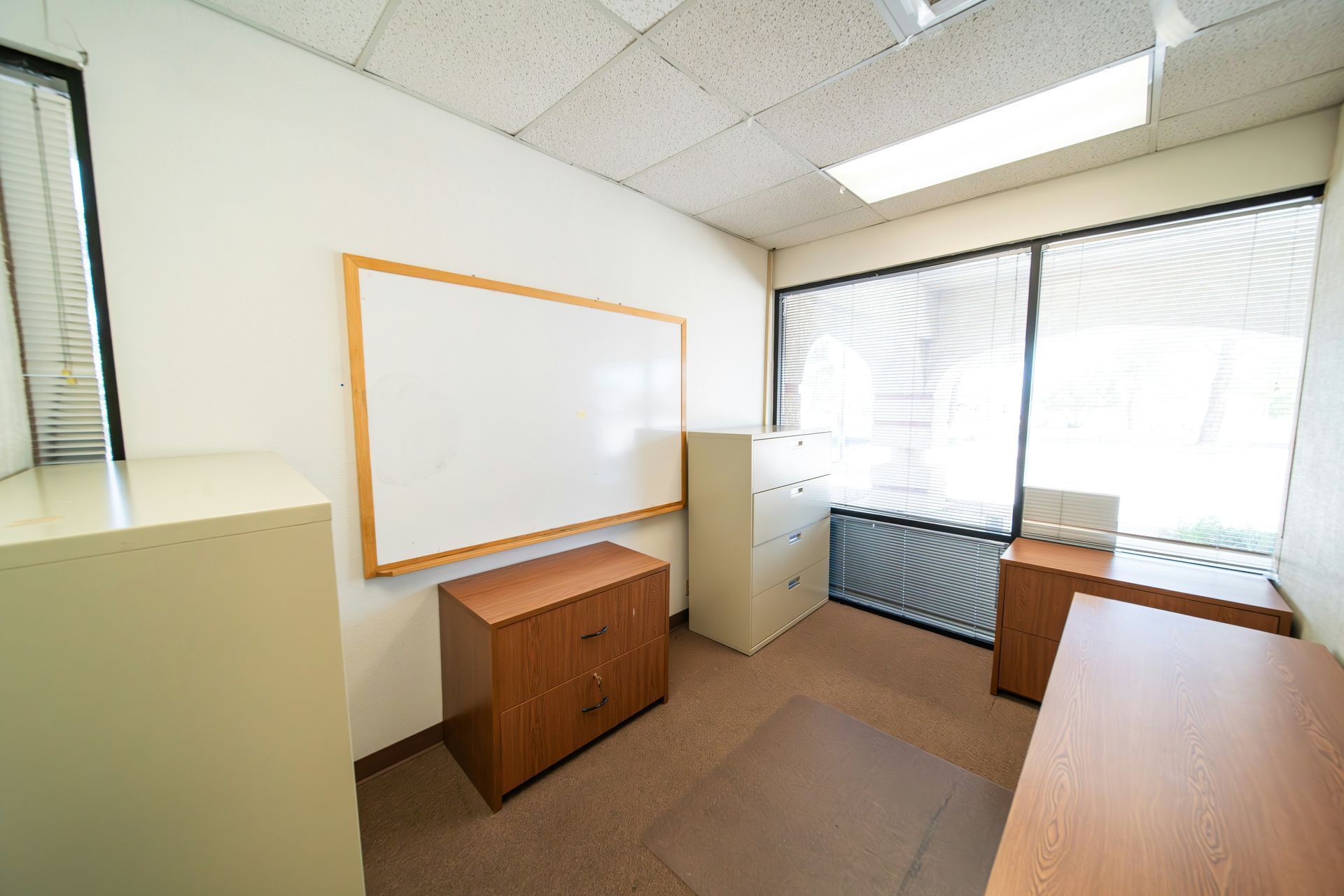 Office with white walls, whiteboard, filing cabinets, desk, and window with blinds.