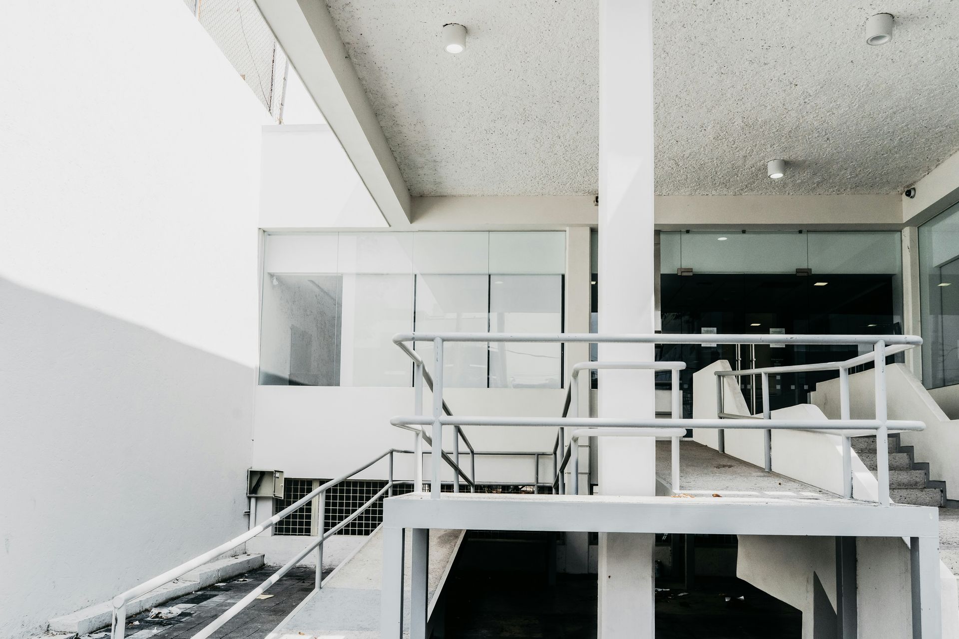 A white, modern building with a ramp and stairs. Glass windows and a white railing are visible.