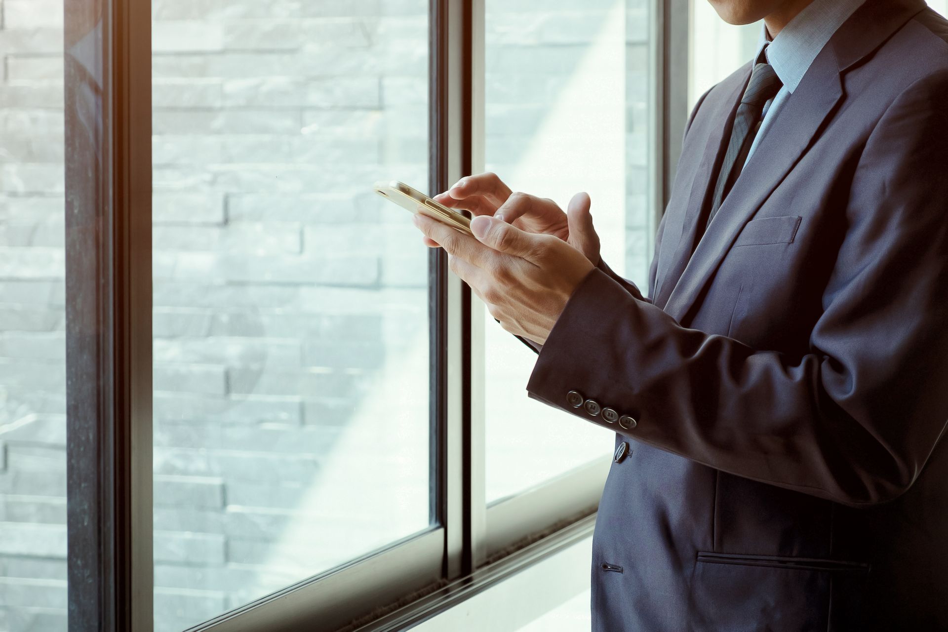 Man in suit using smartphone near a window.