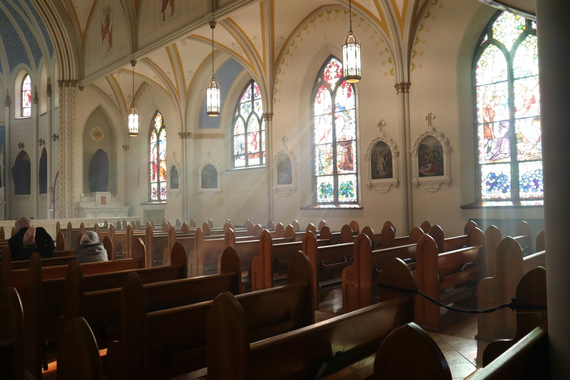 Wooden church pews in a dimly lit room, with a beam of light shining across them.