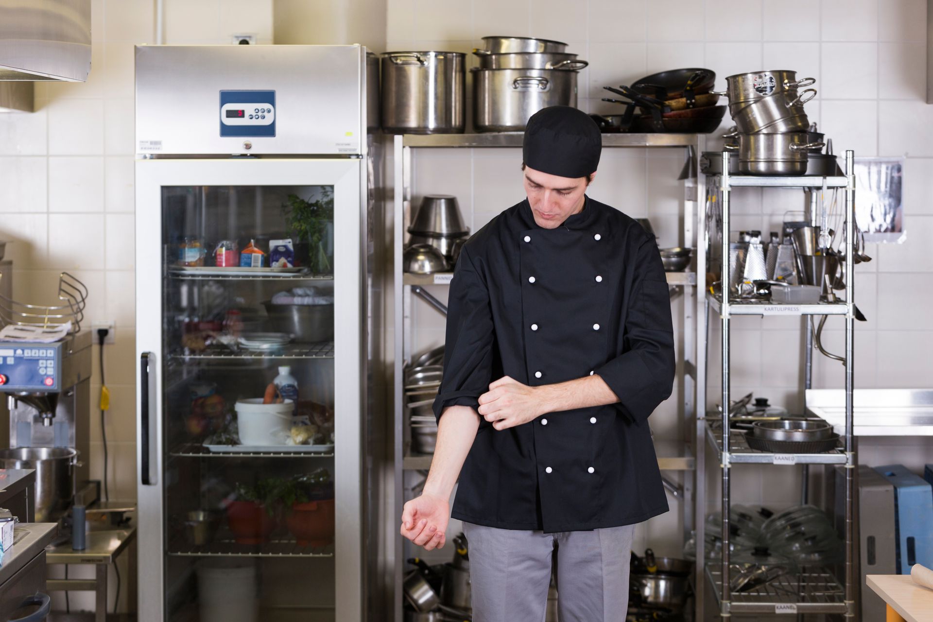 Chef in black uniform rolling up sleeve in kitchen.