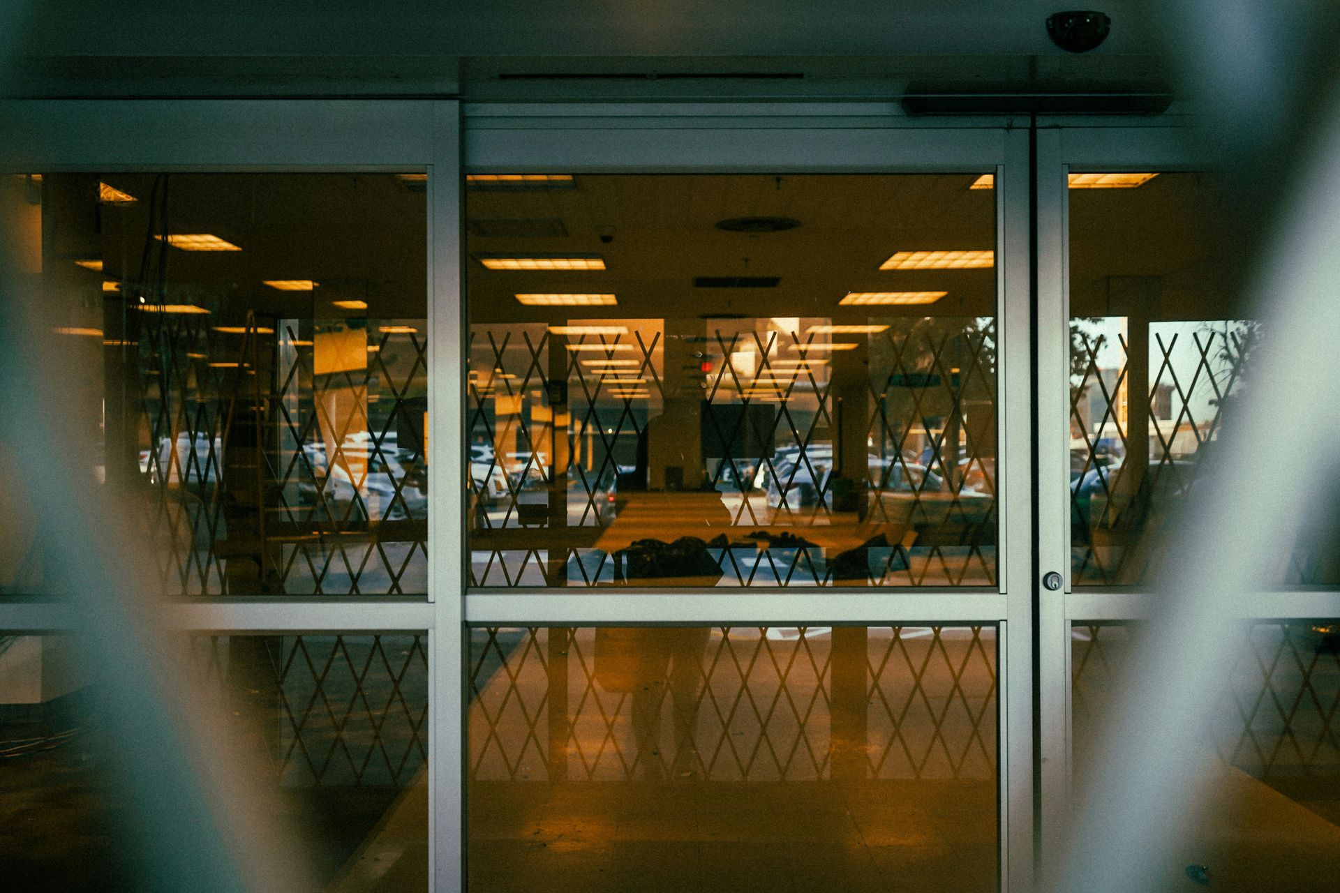 Closed store entrance with security gates; lights on inside, creating reflections.