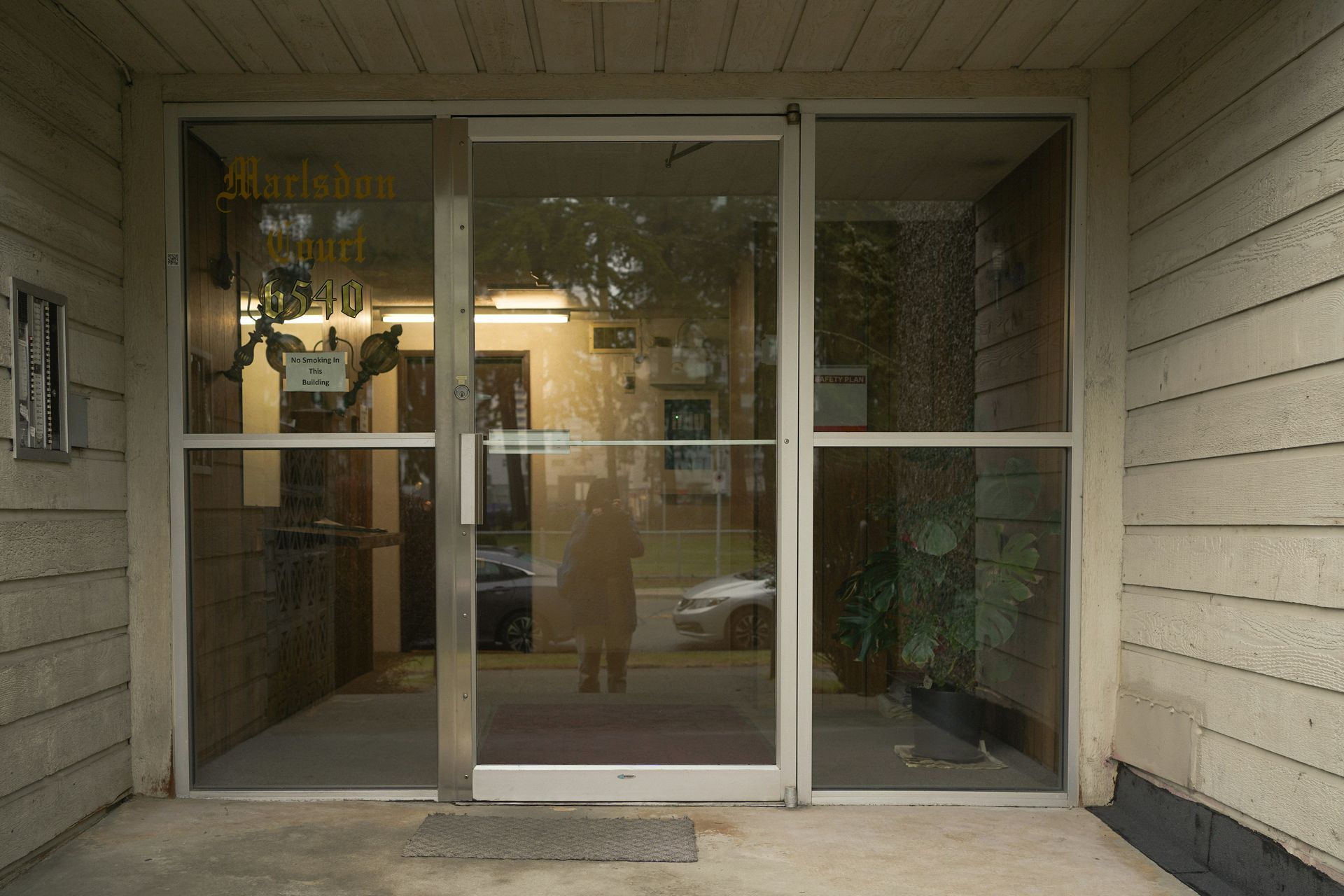 Glass front door of a building; a person's reflection is visible.