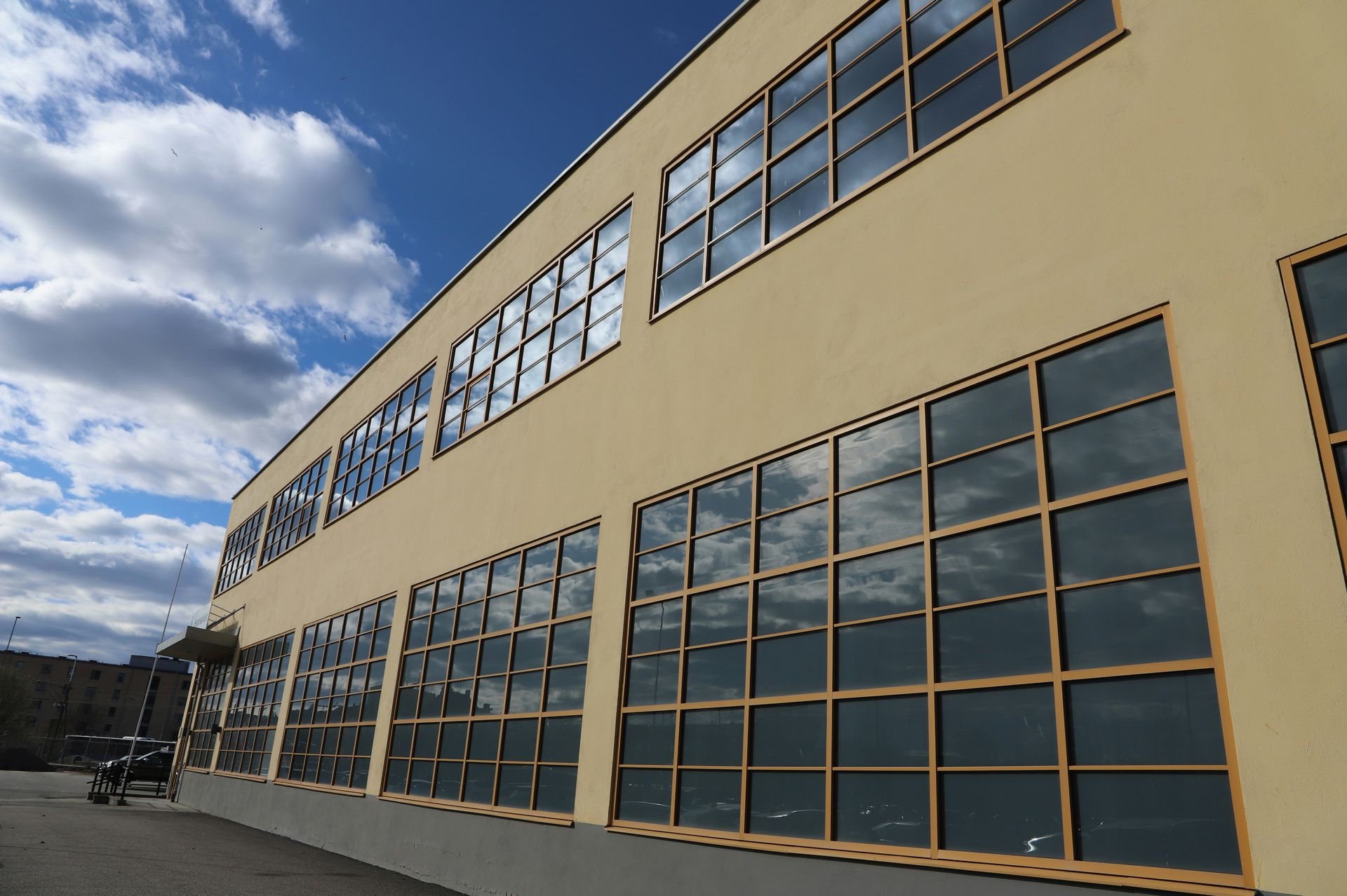 Beige building with large grid windows against a blue sky with clouds; exterior shot.