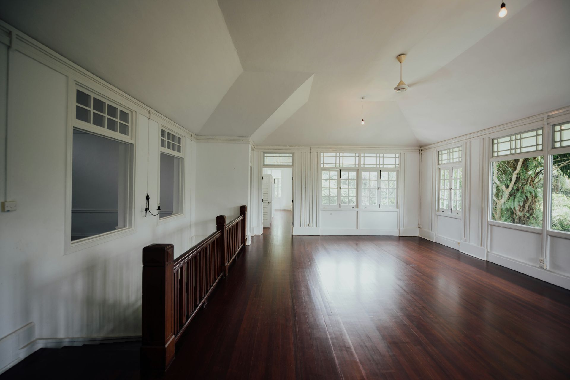 Empty, spacious room with dark wooden floor, white walls, and large windows; natural light.