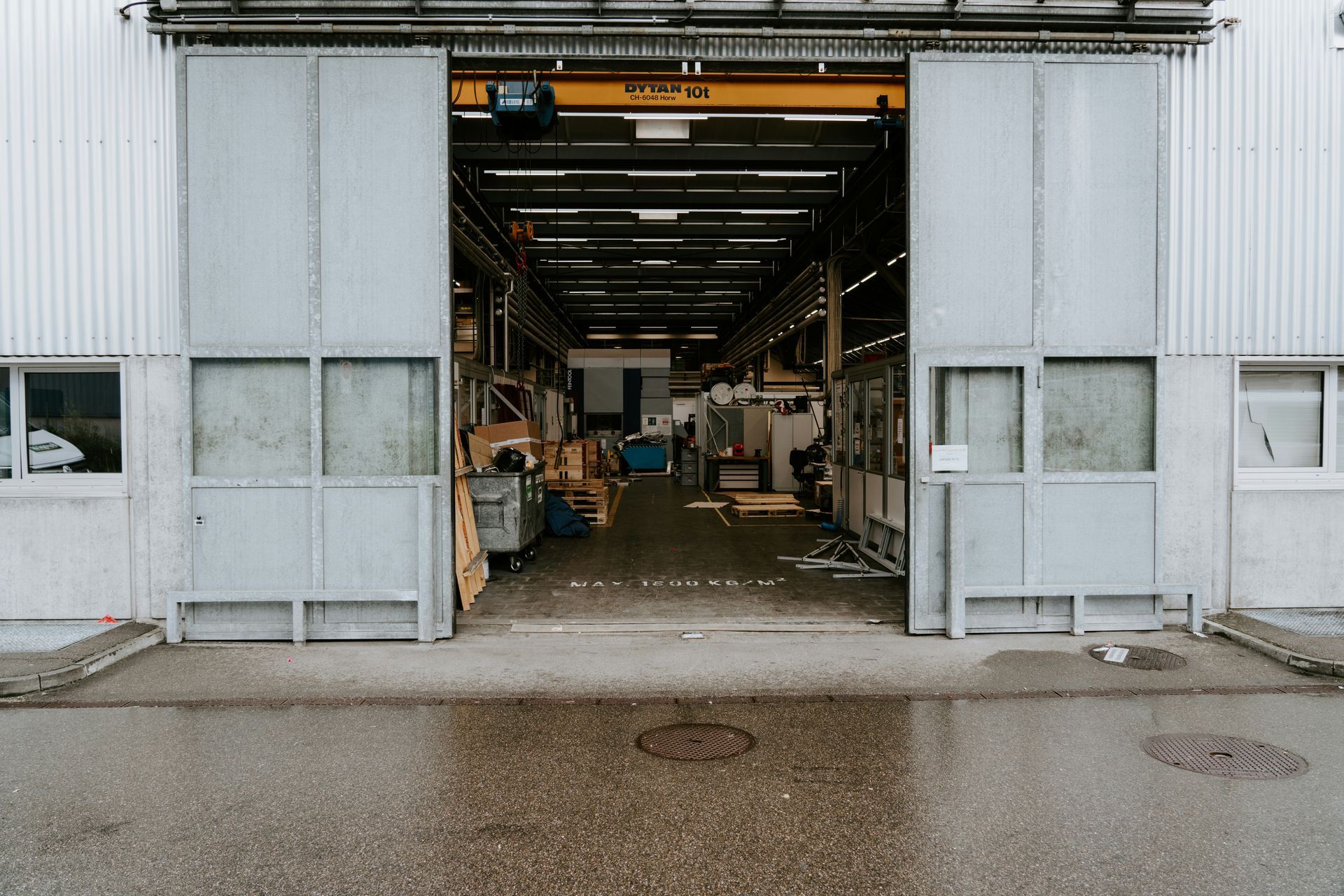 Exterior view of a factory with open sliding doors, revealing the interior. Gray and white building, overcast.