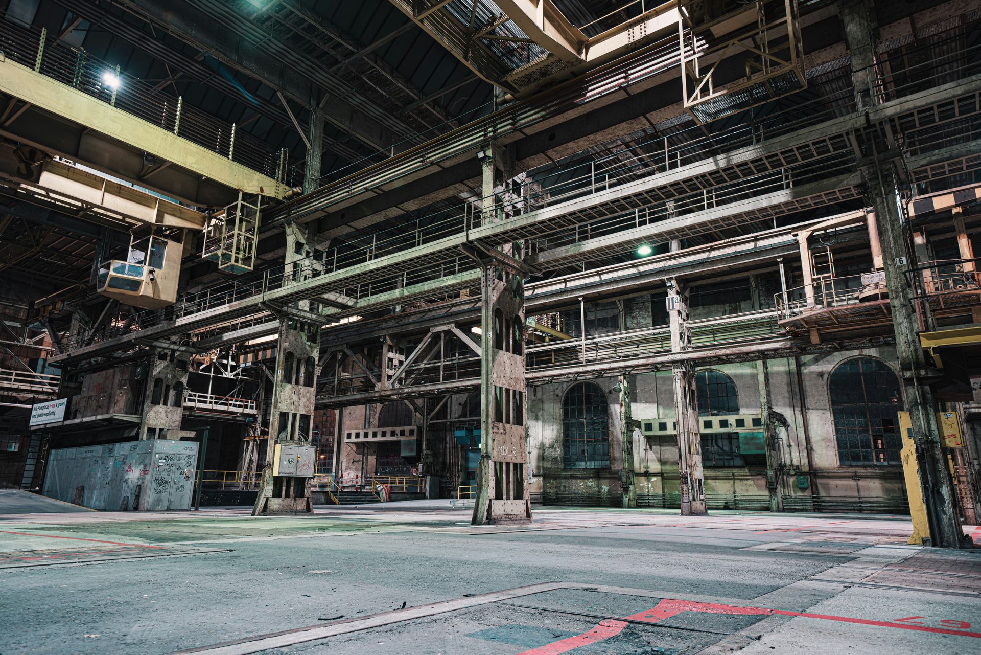 Large, empty industrial space with metal framework, aging walls, and concrete floor.