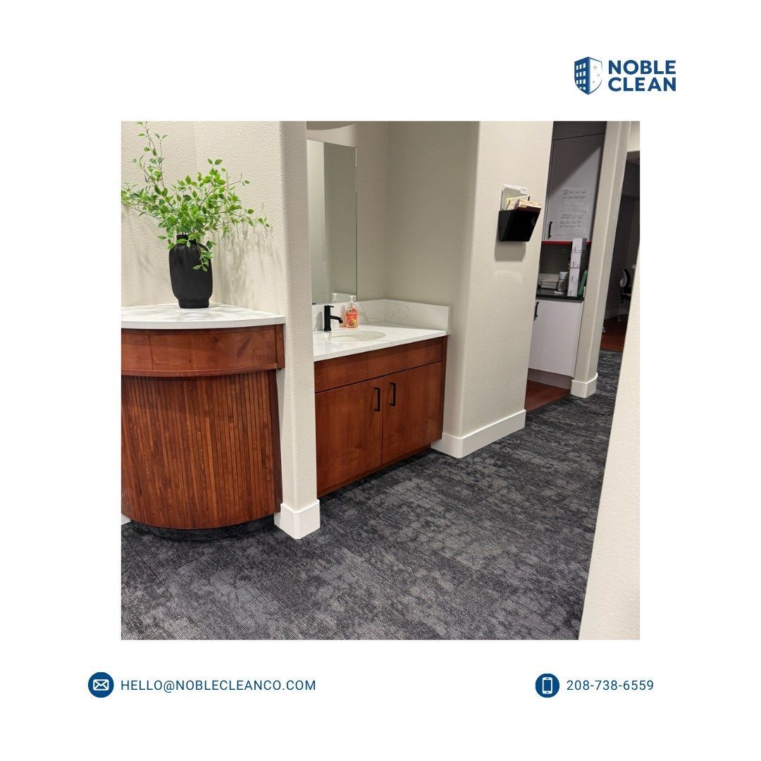 A clean office vanity area with a wooden cabinet, white countertop, a green plant, and dark gray carpet.