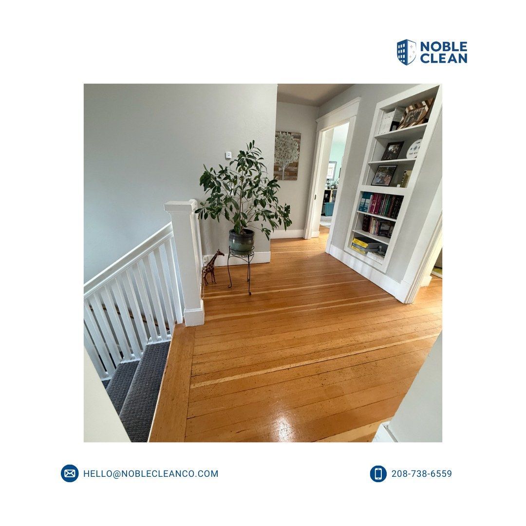A hallway featuring polished wood floors, a white staircase railing, a potted plant, and a white built-in bookshelf.