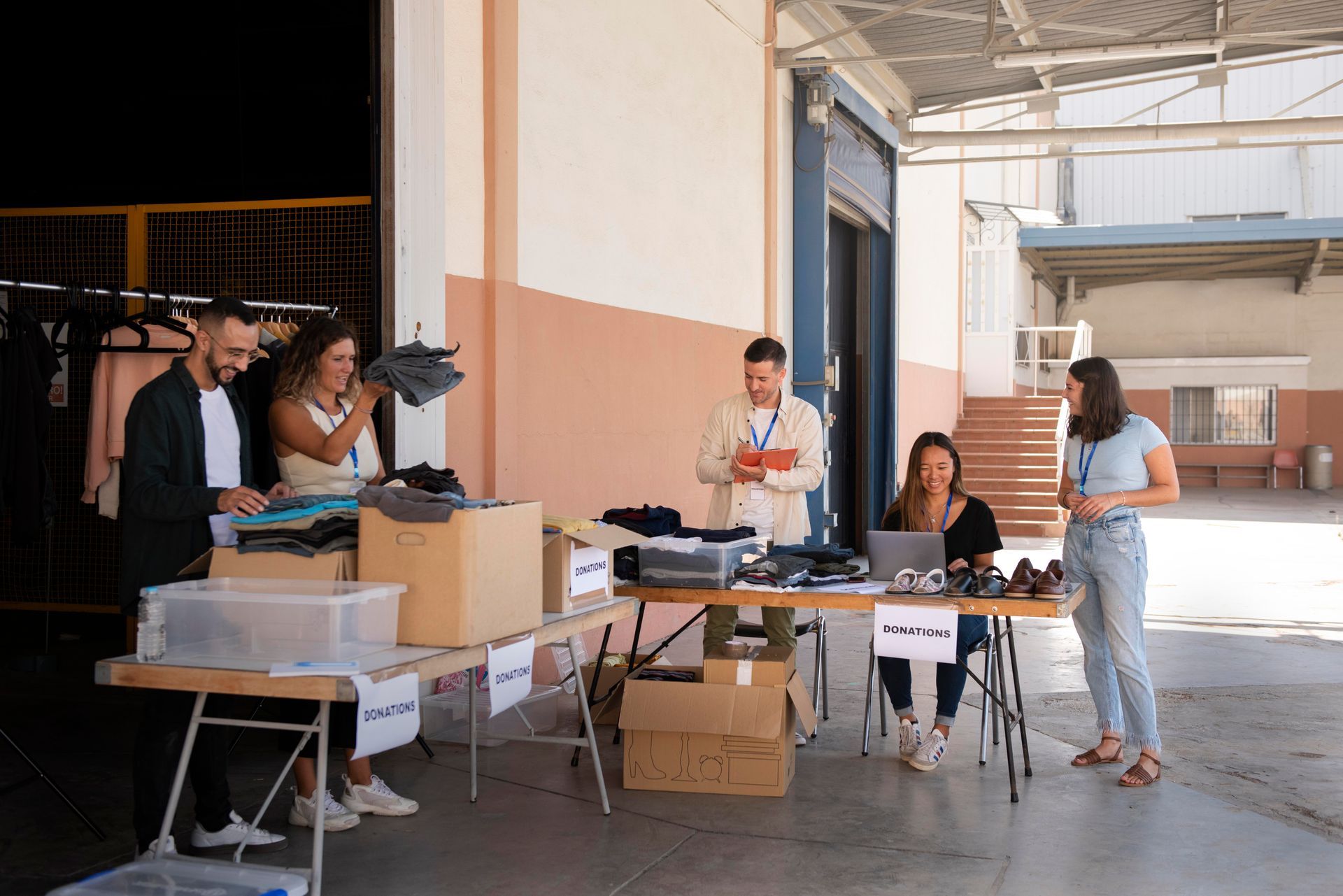 People sorting clothing donations at a table in an outdoor warehouse area.