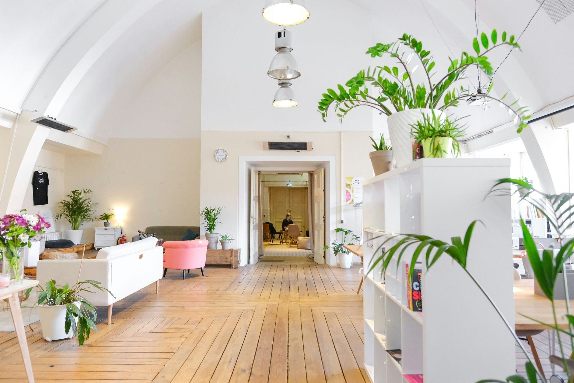 Spacious interior with white walls, wooden floors, plants, and a long hallway leading to another room.