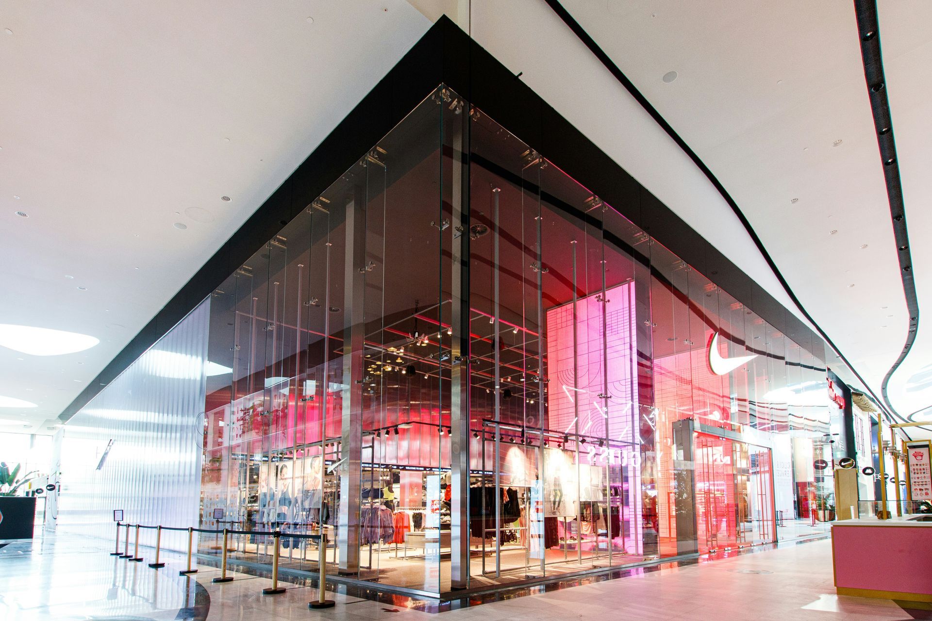 Nike store with glass facade, visible merchandise, and pink and red interior lighting.