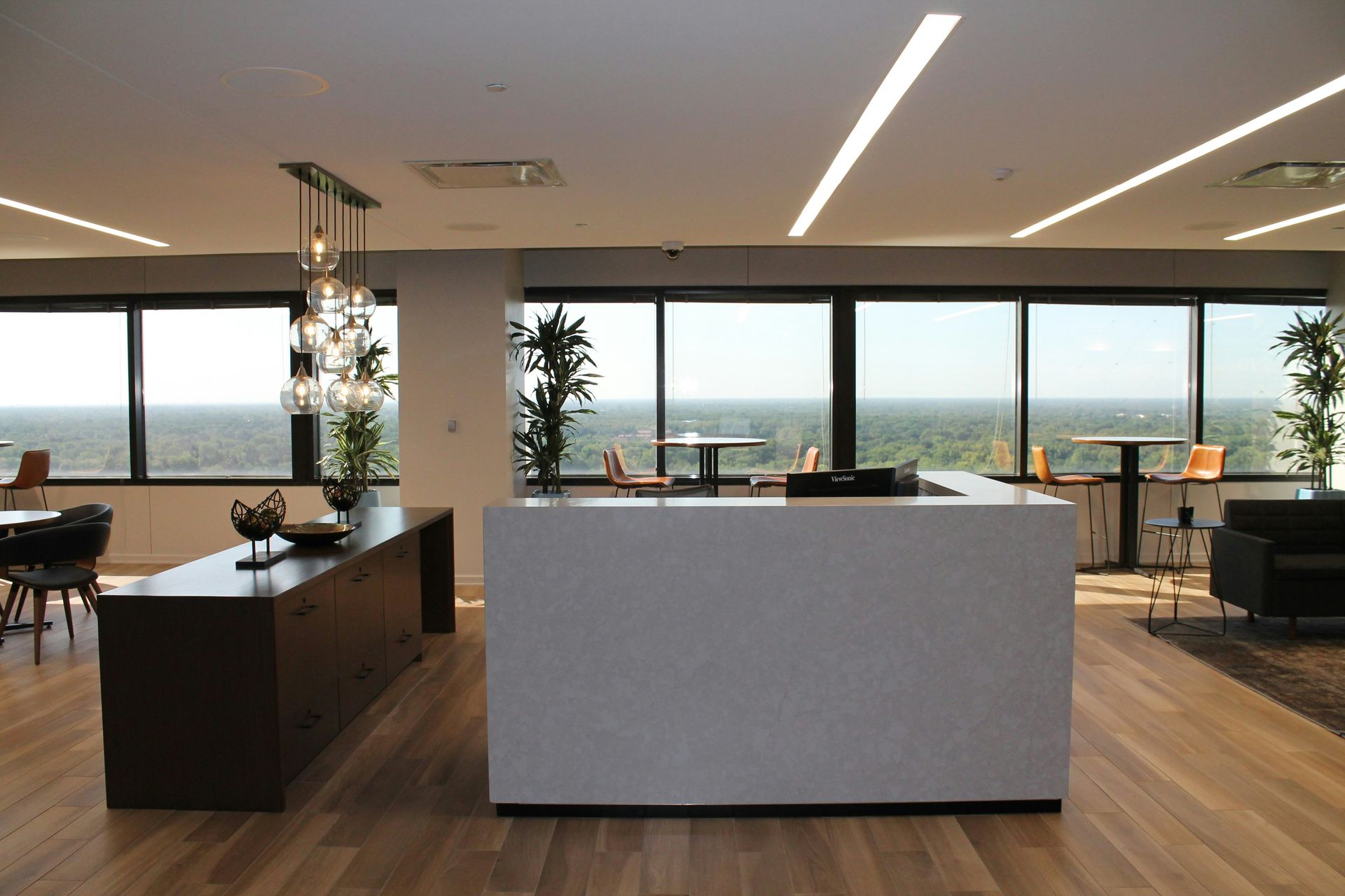 Modern office lounge with a white and brown bar, large windows, and forest view.