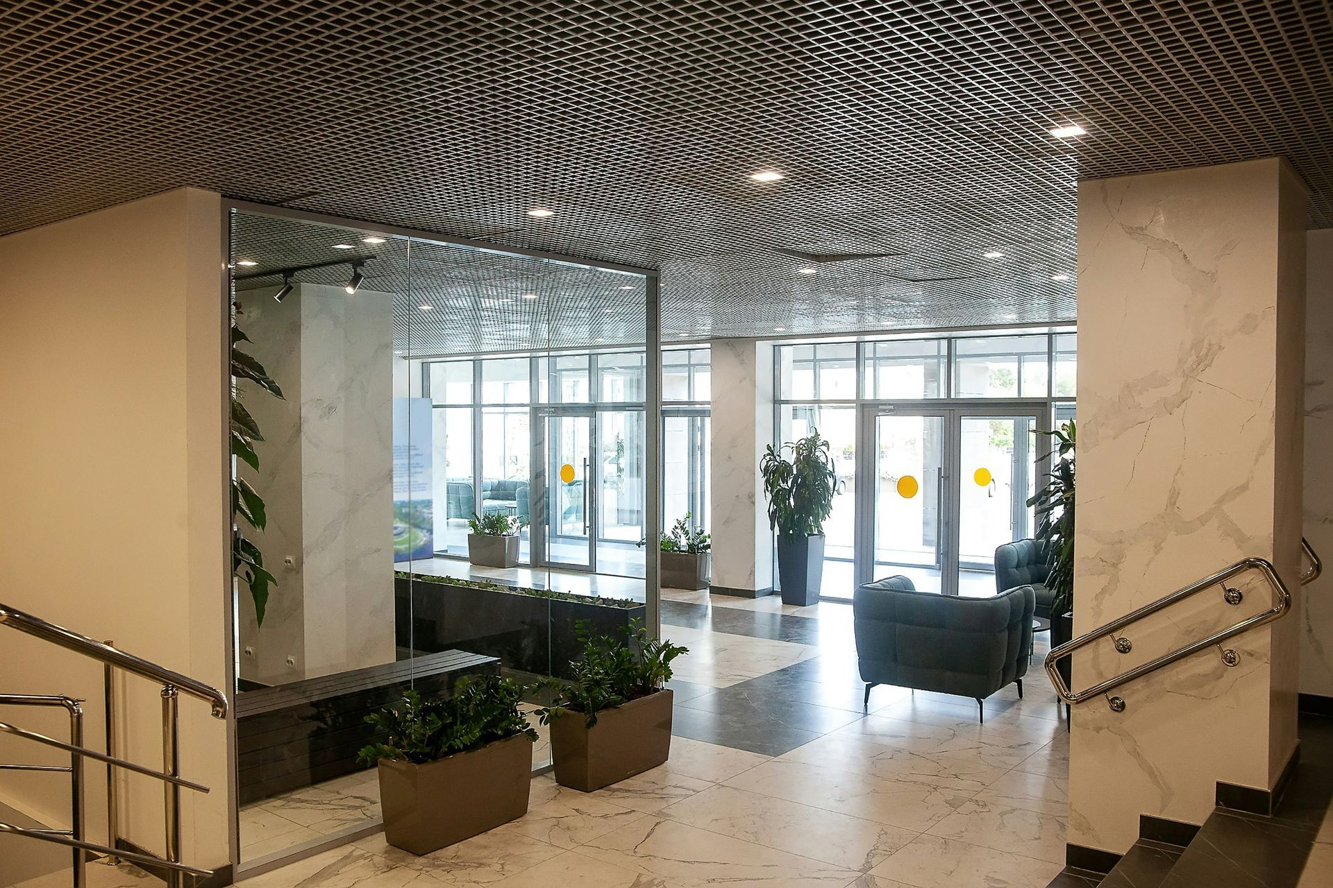 Lobby with marble columns, reflective mirror wall, plants, and glass doors leading outside.