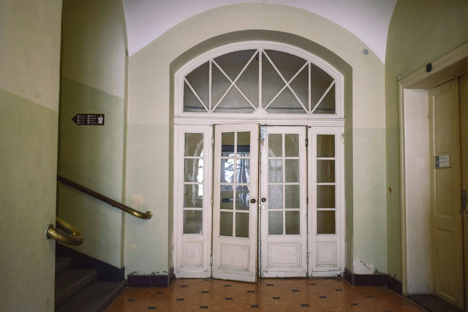 Interior hallway with white doors, a staircase, and an elevator. Light green walls and arched doorway.