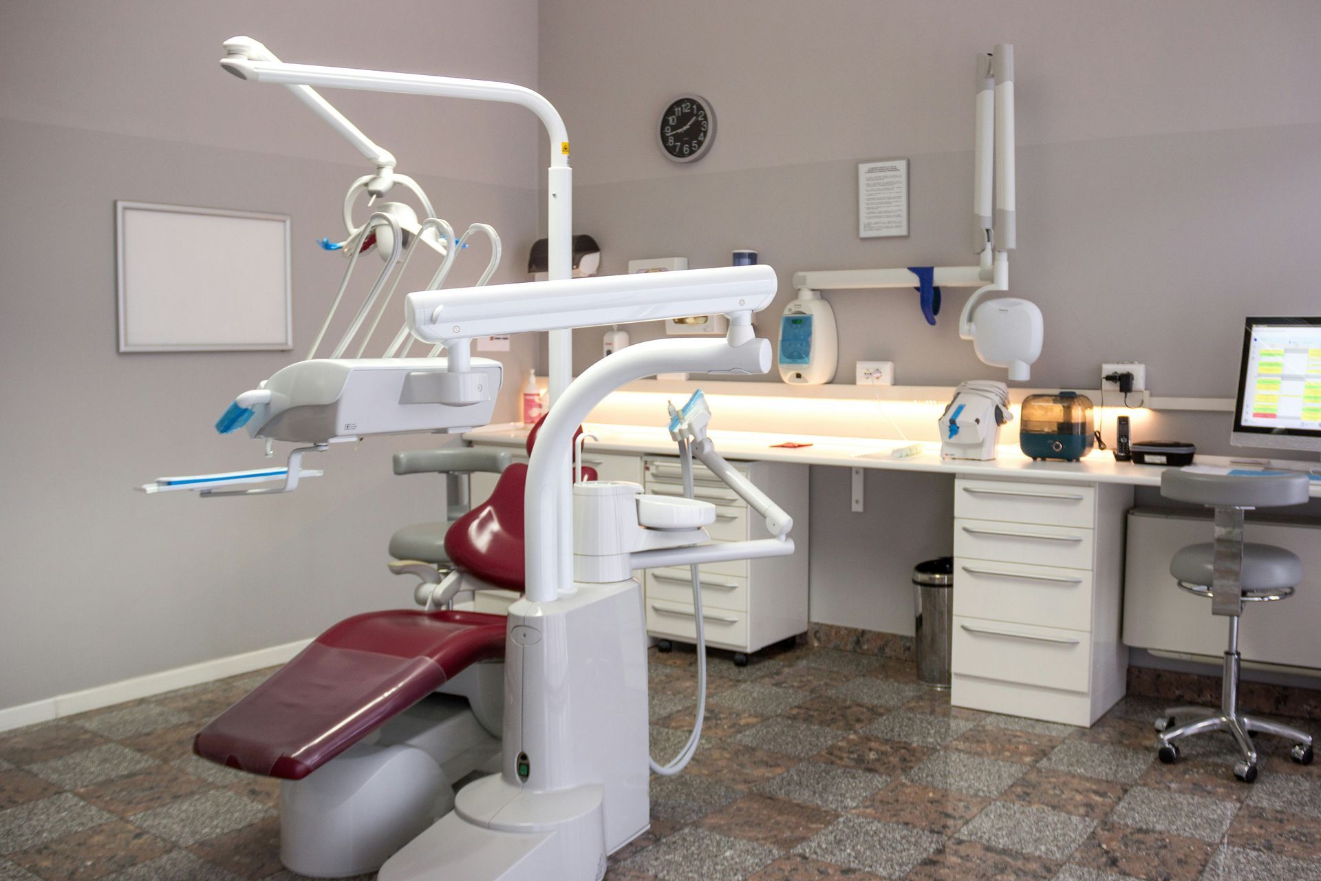 Dentist's office with a maroon dental chair, white equipment, and a computer.
