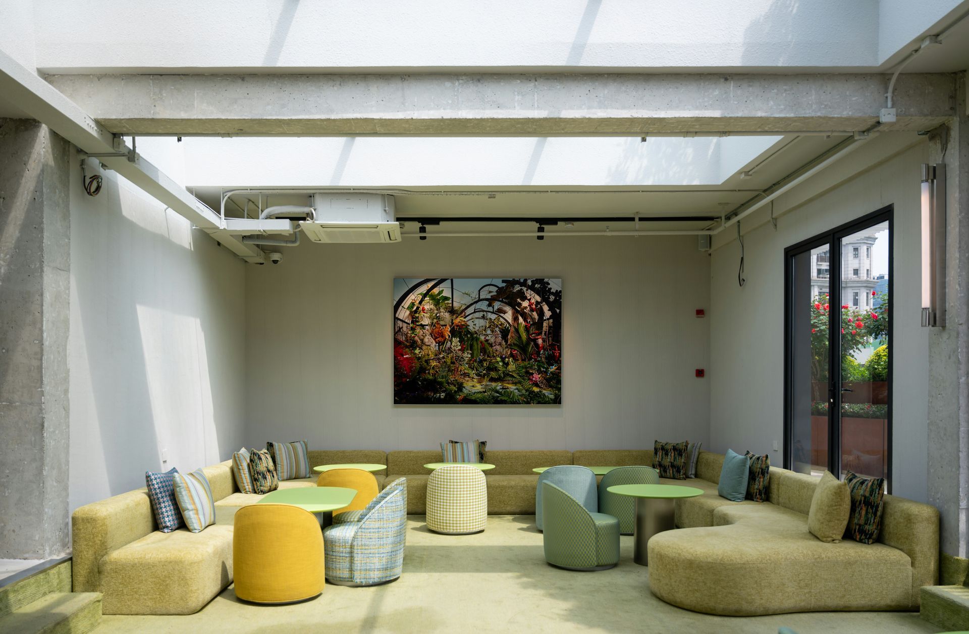 A light-filled lounge area with curved yellow couches, a colorful painting, and a glass skylight.